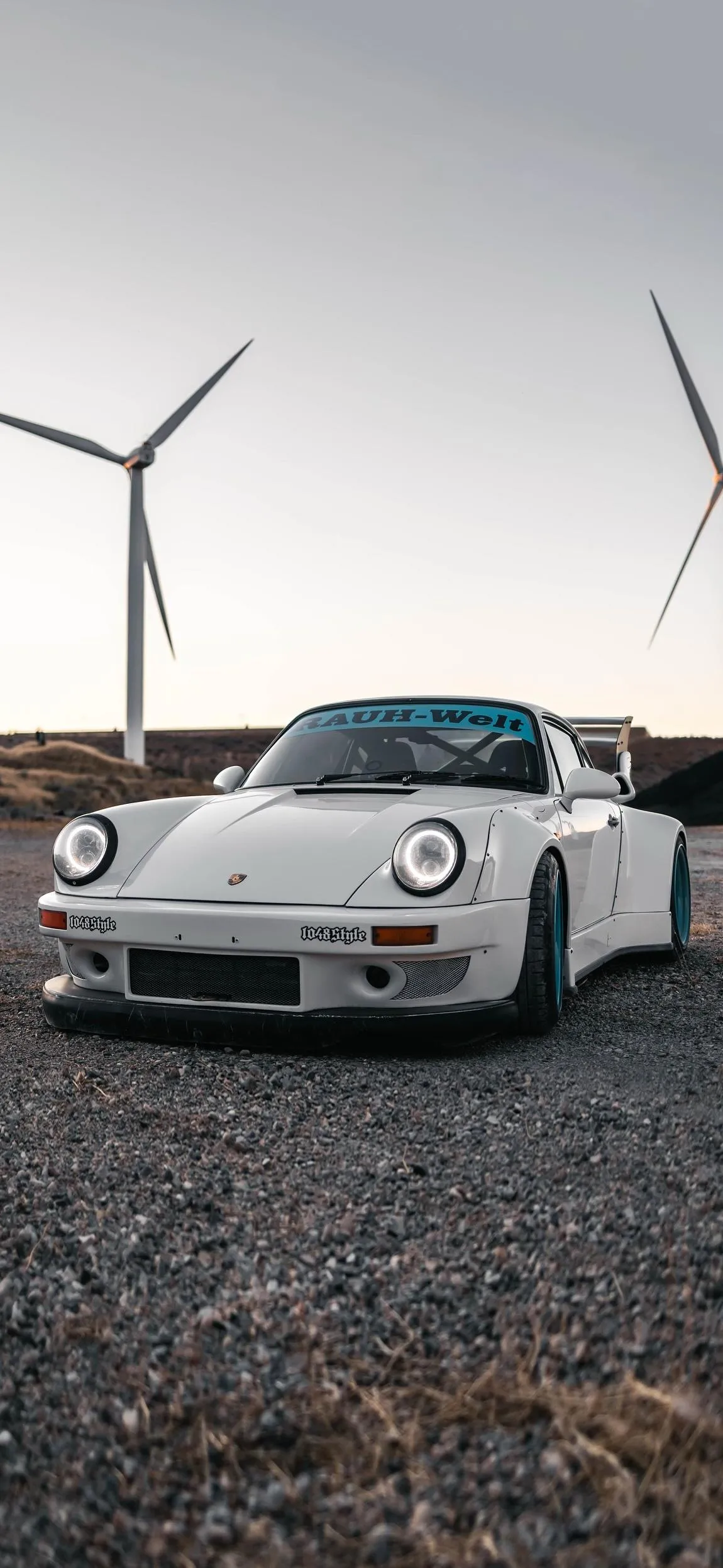 White Car Parked On Gravel Road Near Wind Turbines