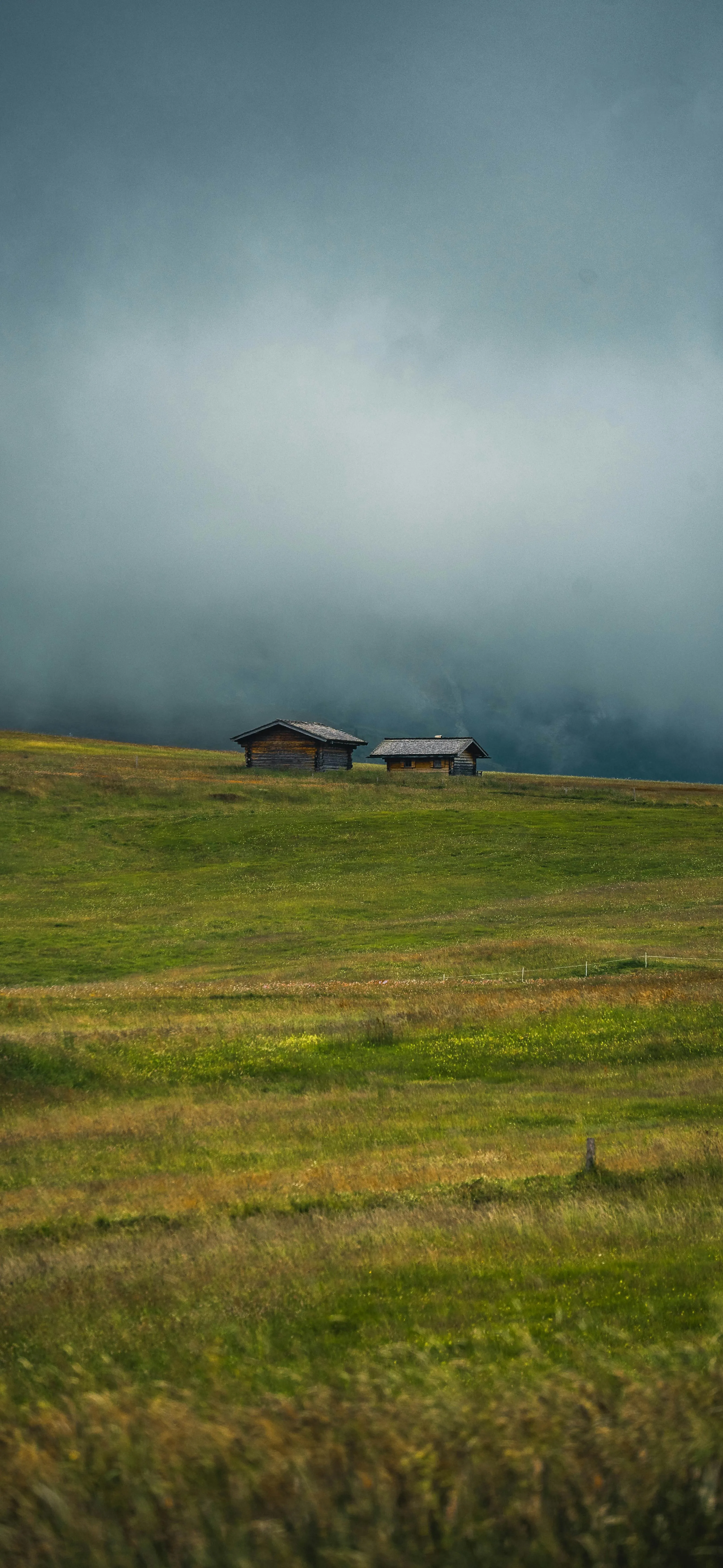Wide Green Field Under Cloudy Sky with Small House Image
