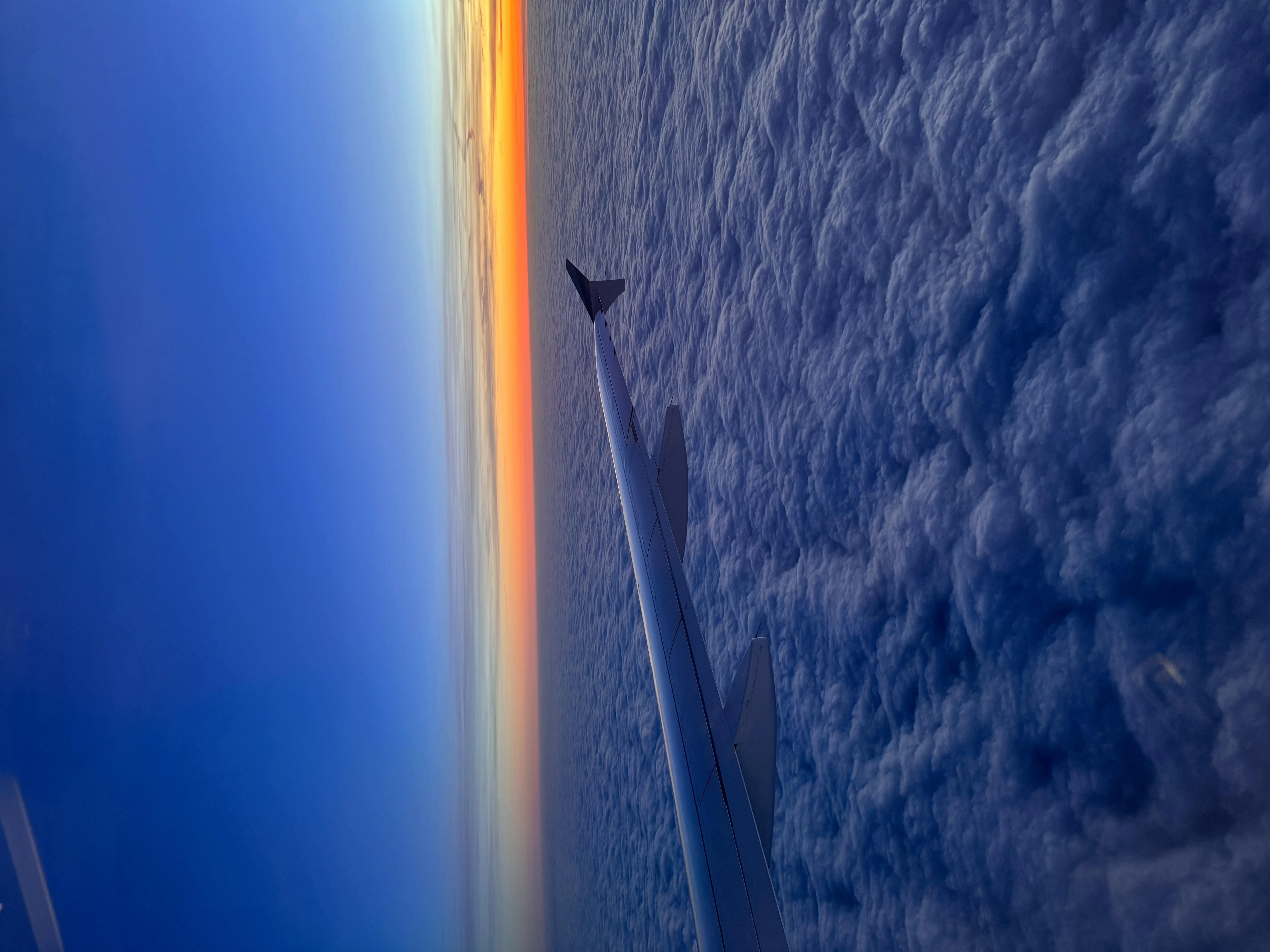 Wing View of Airplane Flying Over Cloudy Sky at Dusk