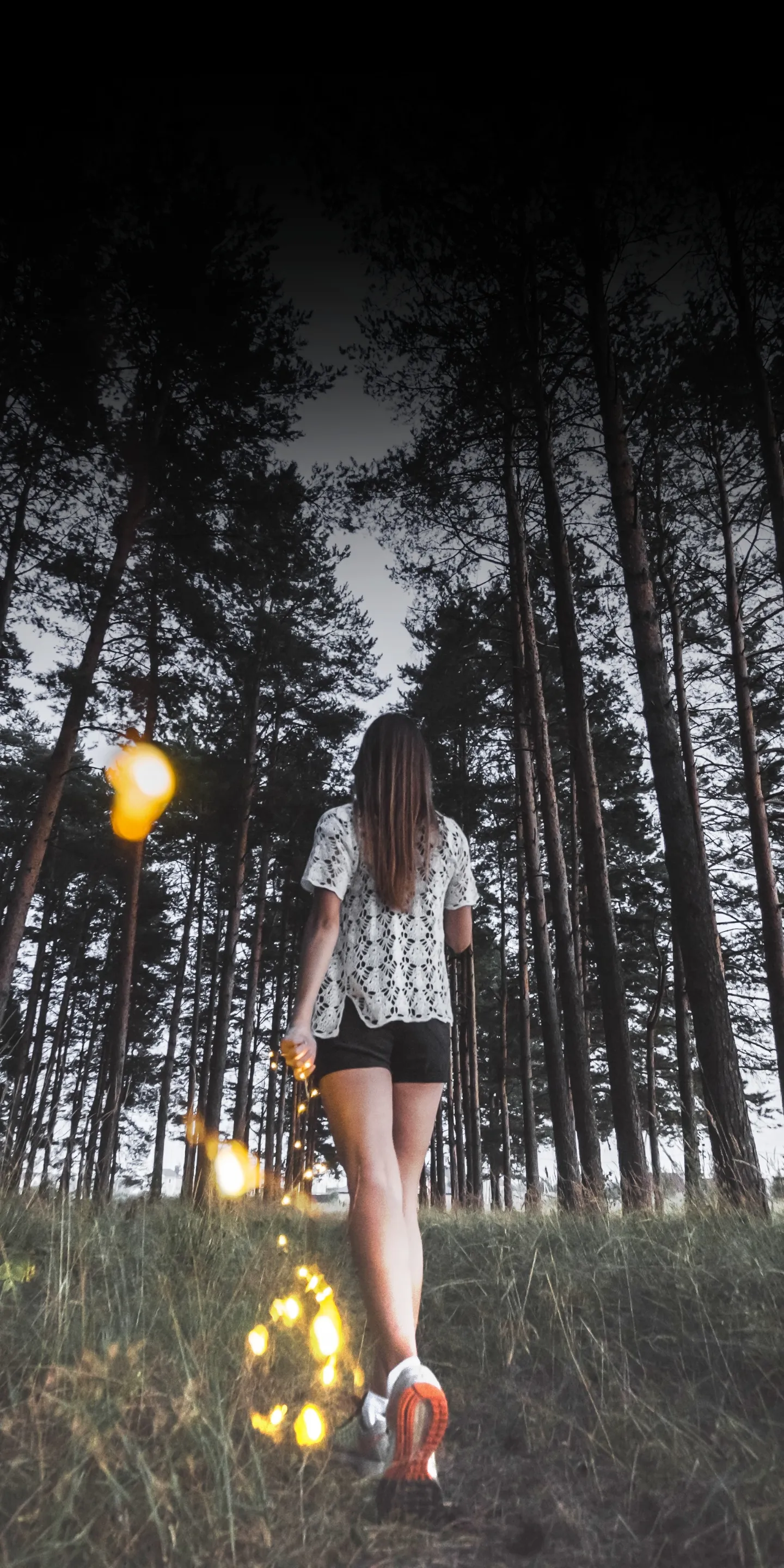 Woman Walking in Dark Forest with Lights in Background