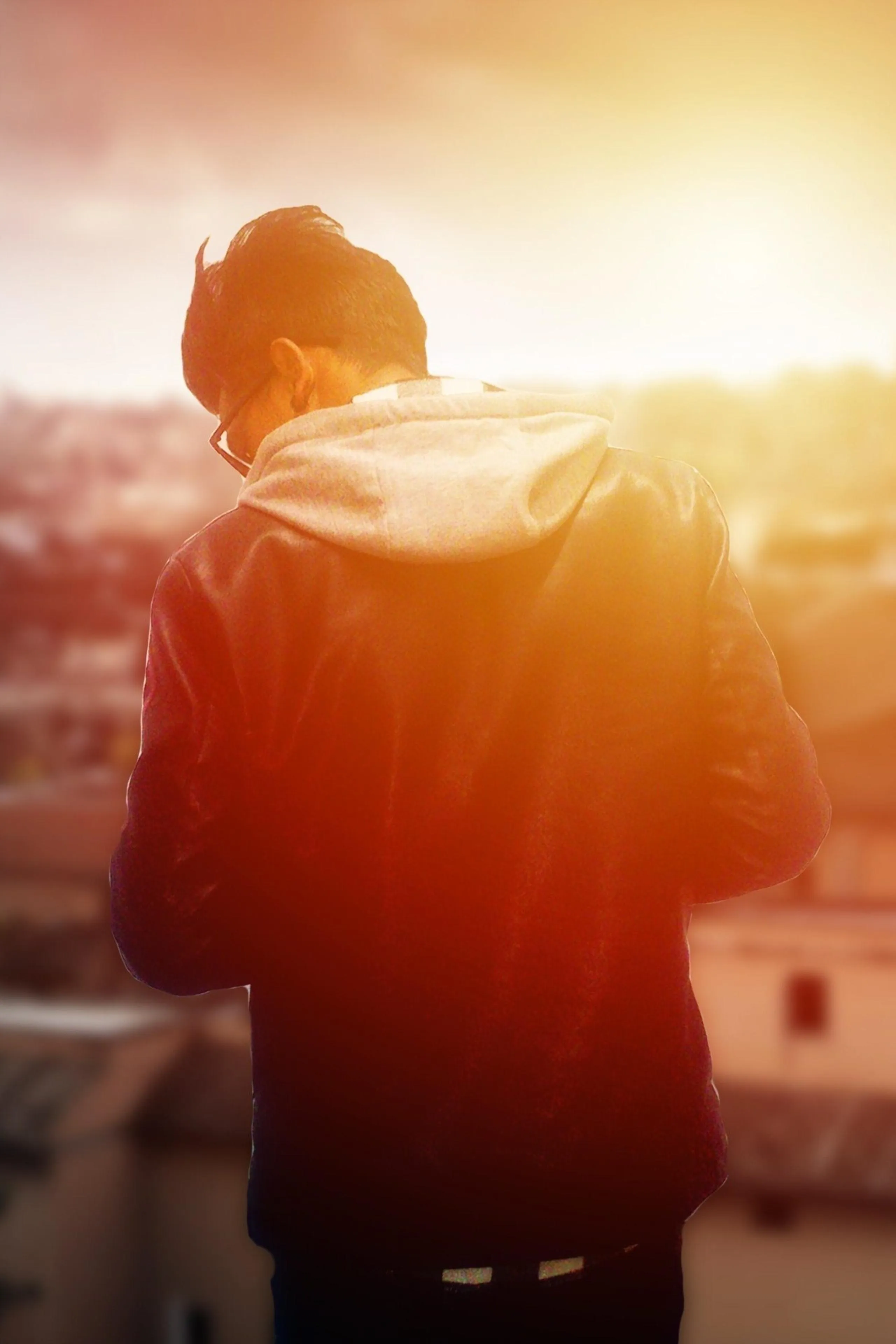 Young Man in Hoodie Watching Sunset Over Urban Cityscape