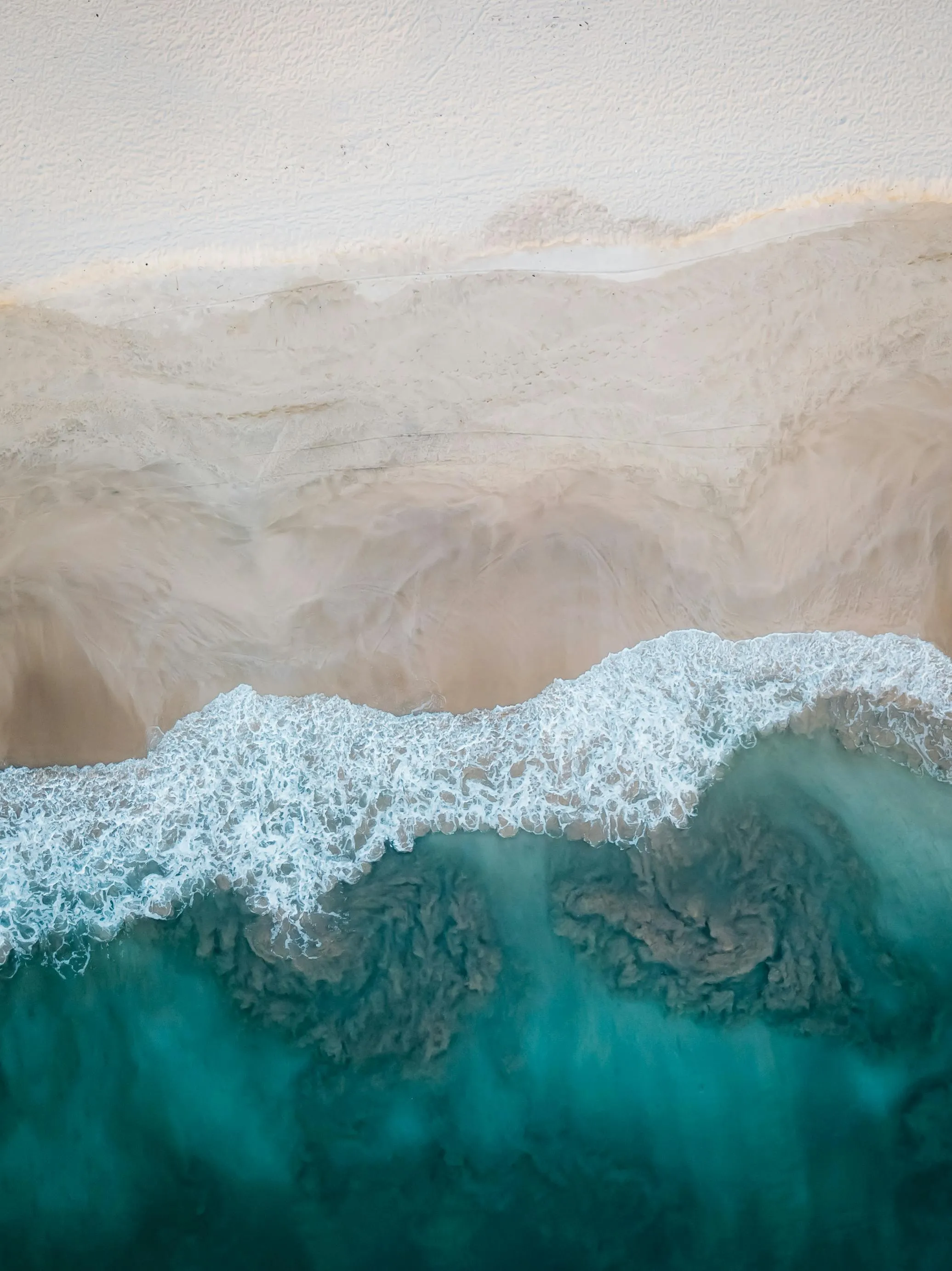 Aerial view of ocean waves crashing onto a sandy shore 4K
