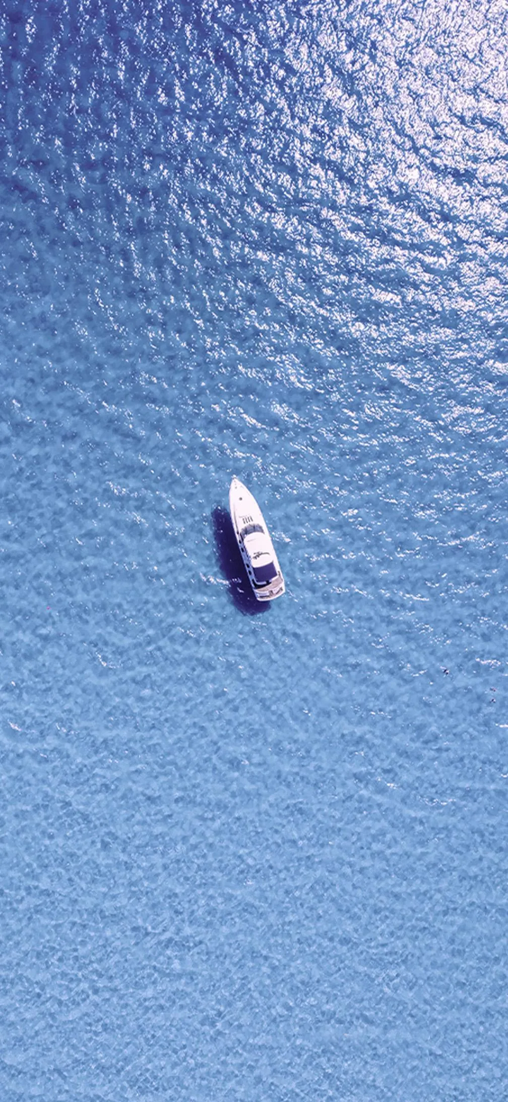 Aerial view of small boat in vast calm blue ocean Wallpaper