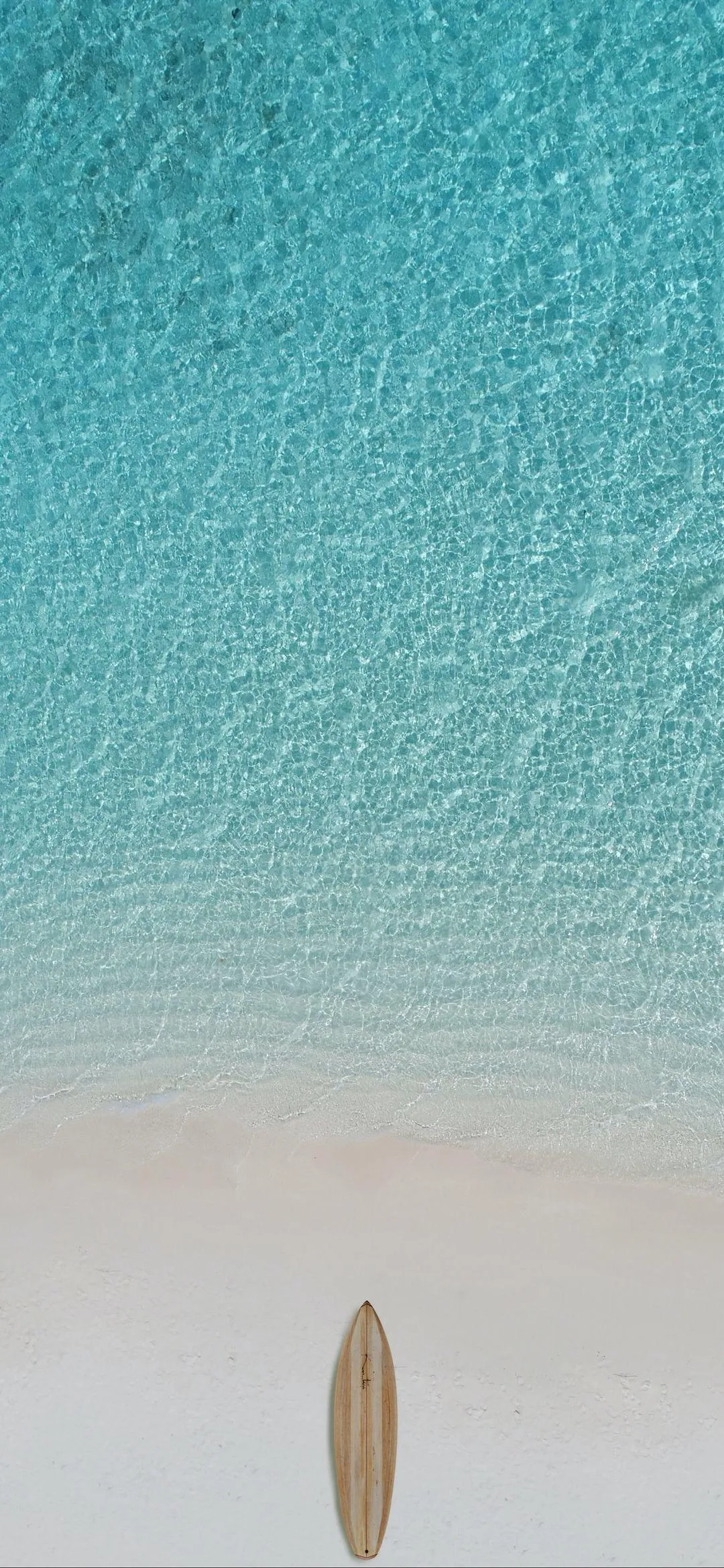 Calm beach with clear blue water and distant surfboard