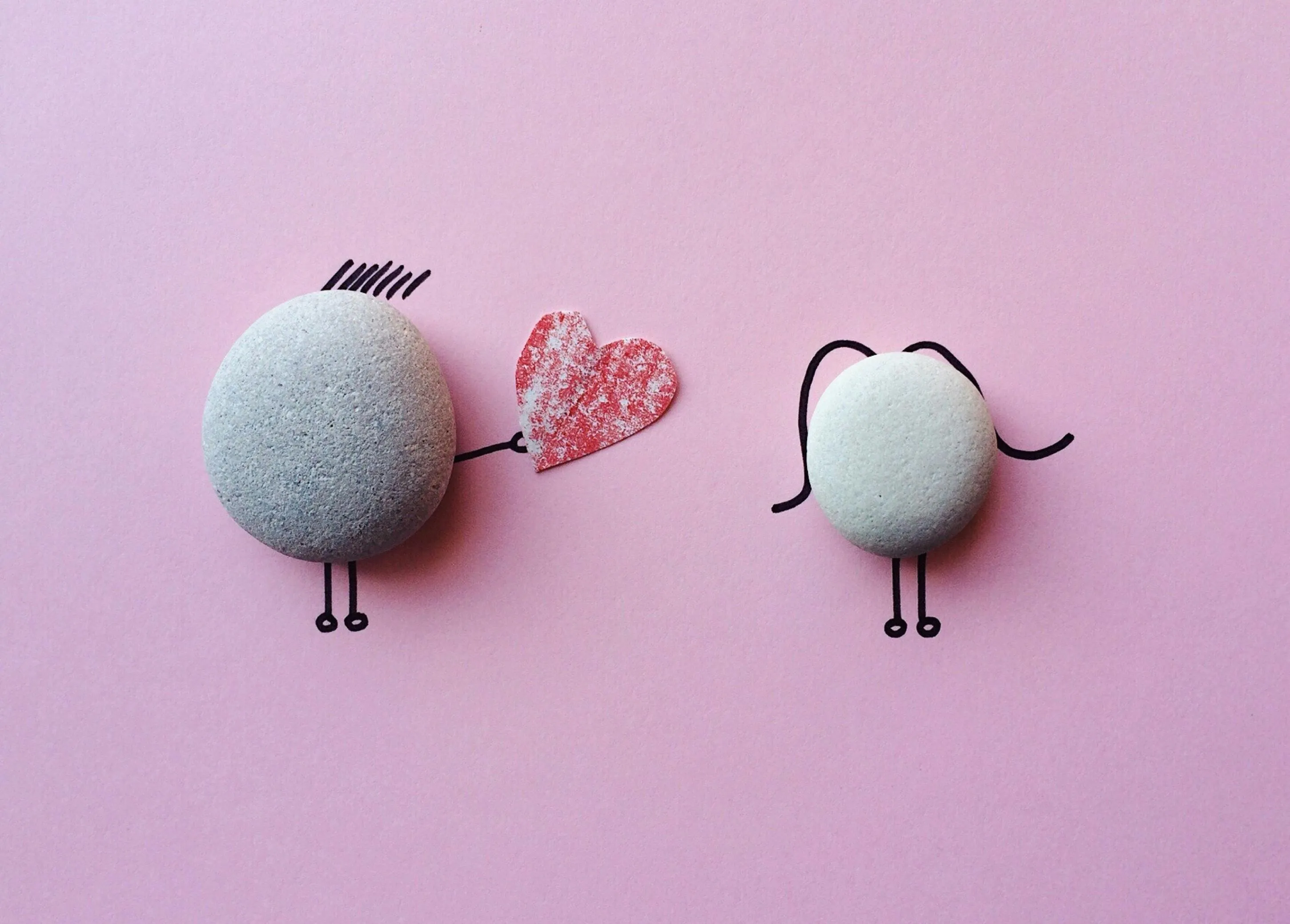 Cute stones with drawn legs holding heart on pink background