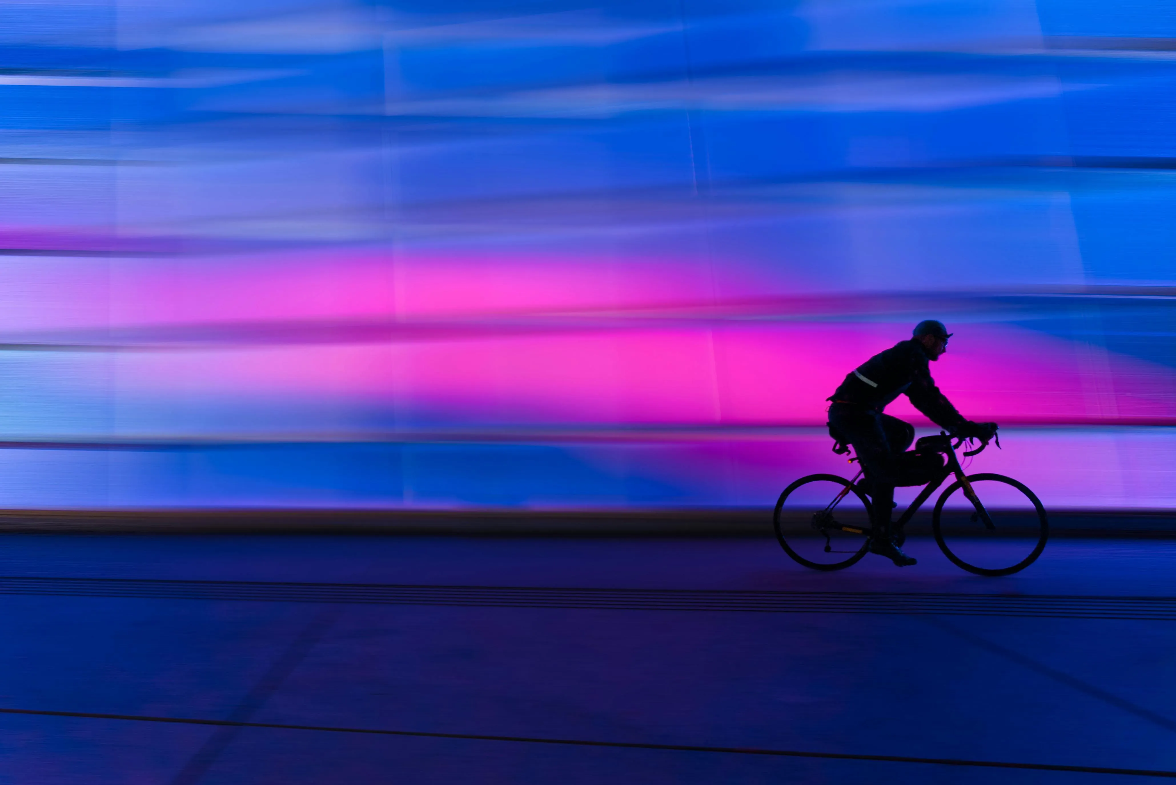 Cyclist riding through a vibrant purple and blue neon wall