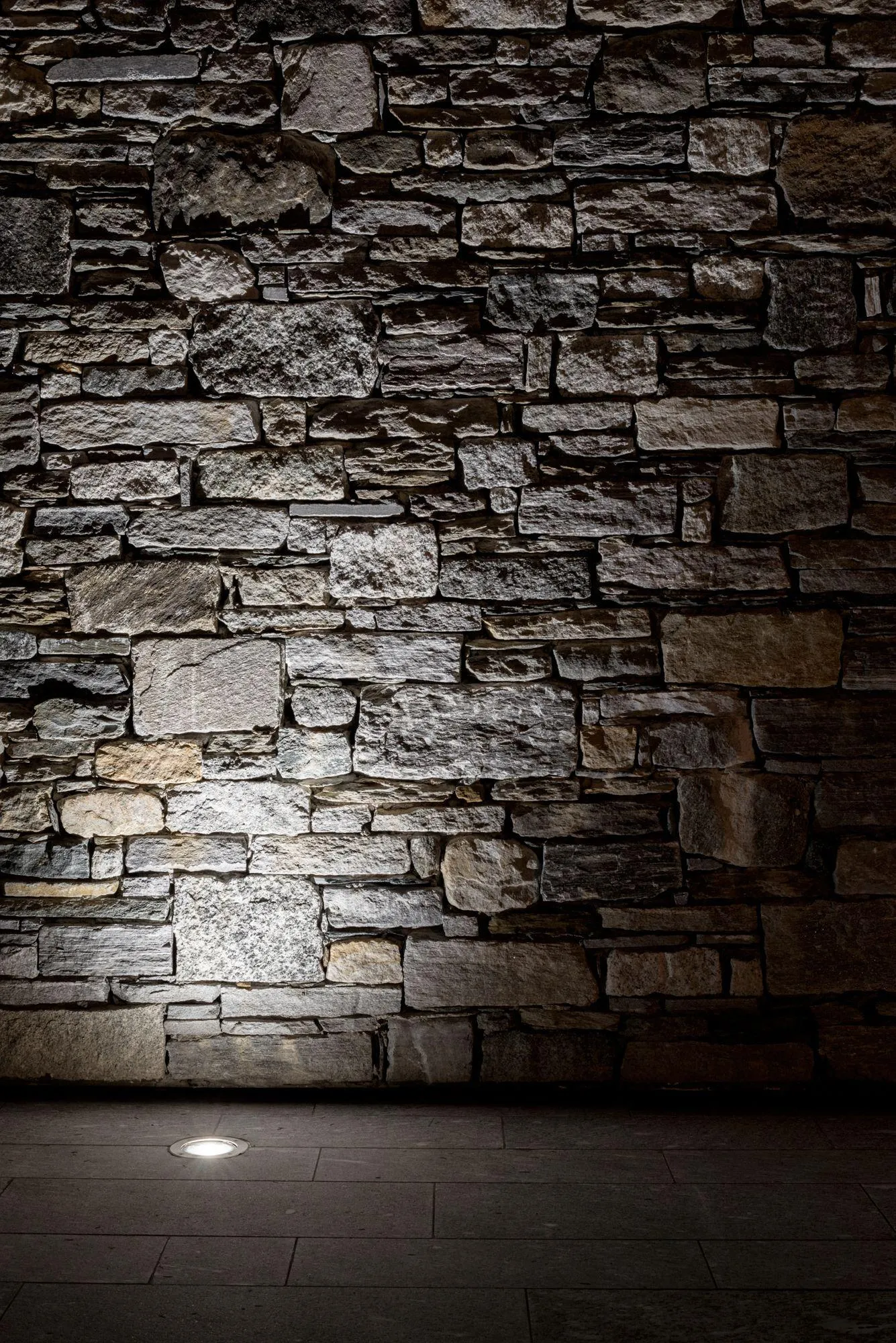 Dimly lit stone wall with a spotlight on the floor Wallpaper