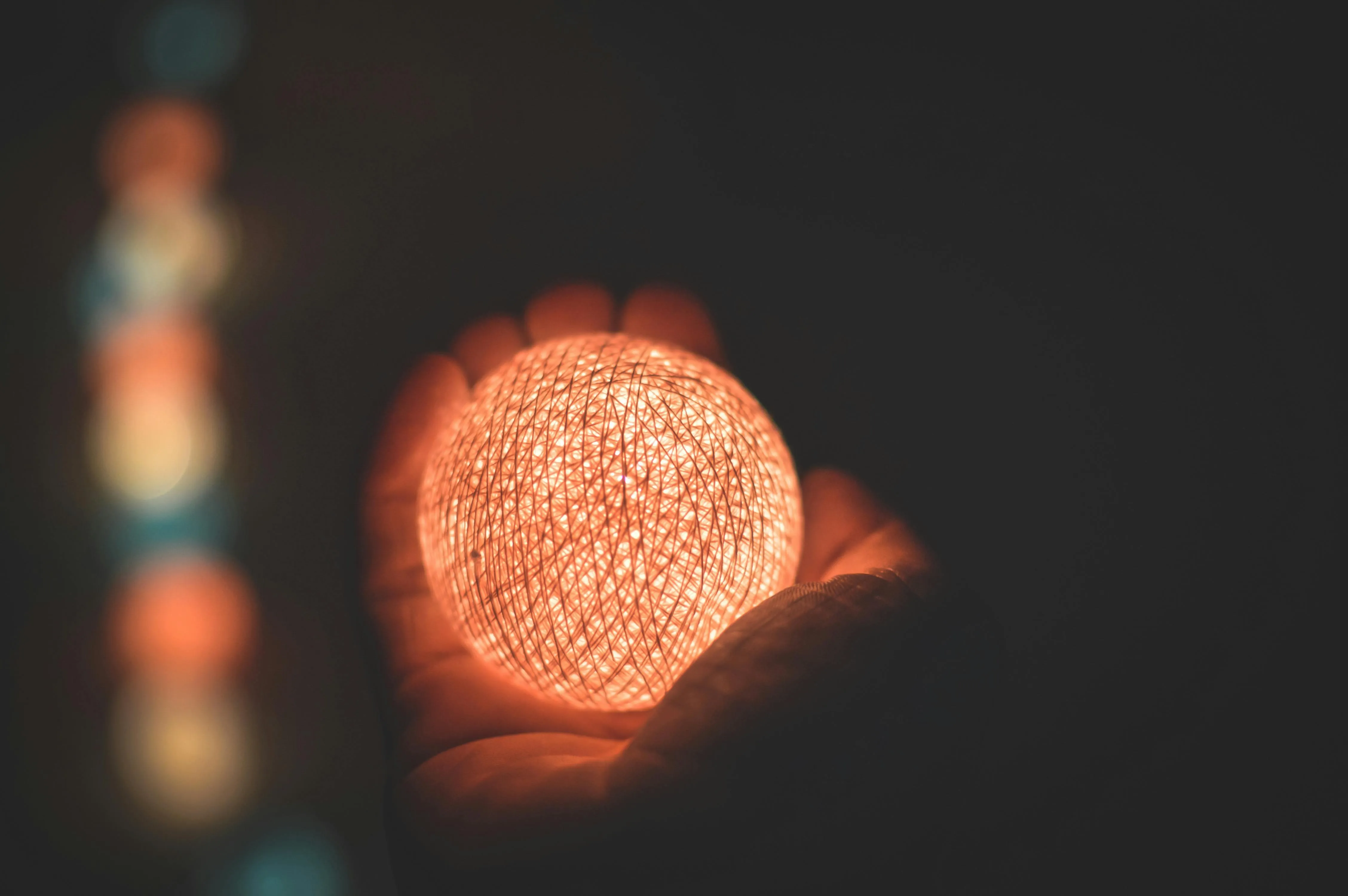 Hand holding a glowing spherical light in a dark setting