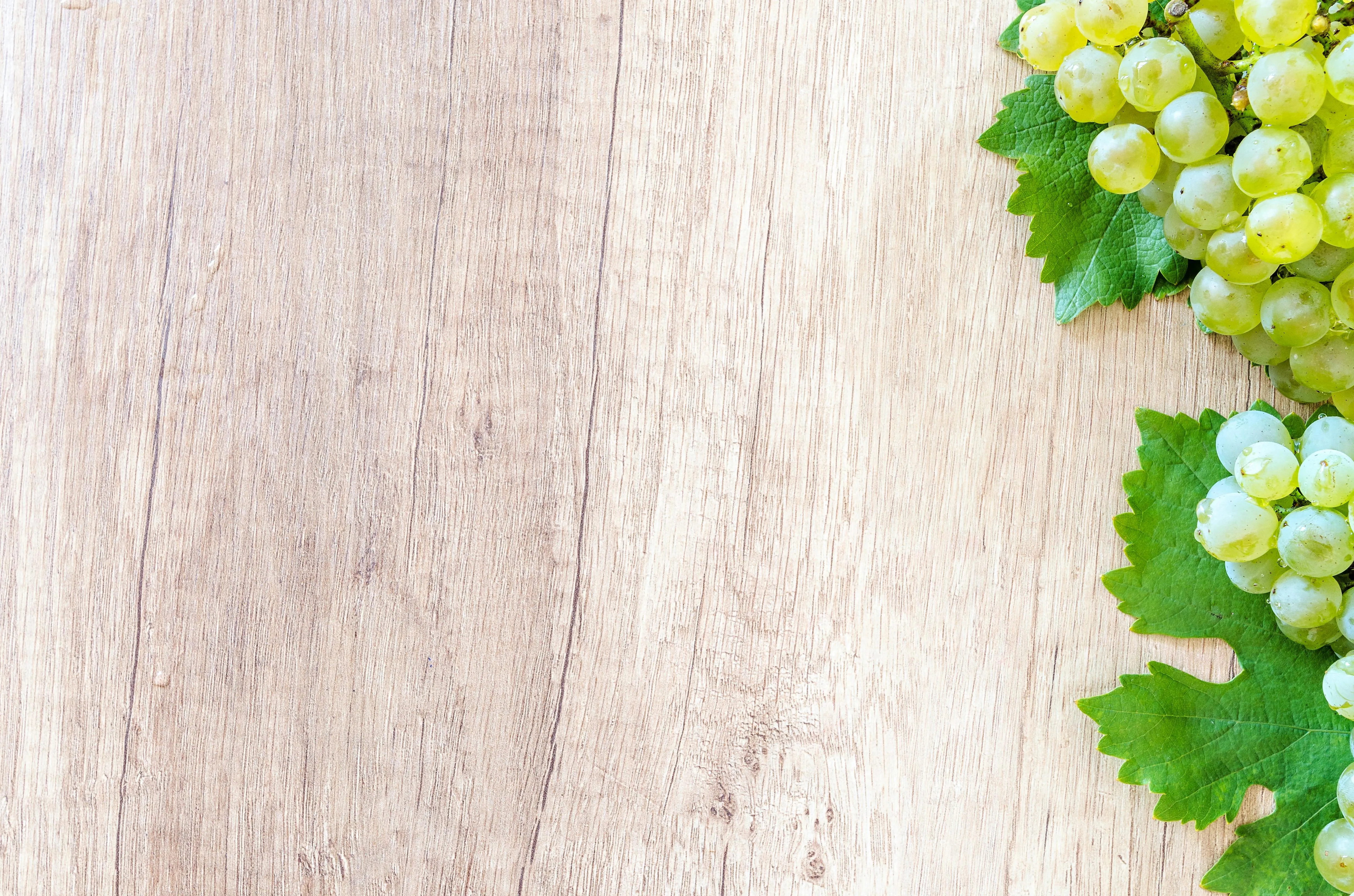Light wooden table with green grapes and leafy decoration