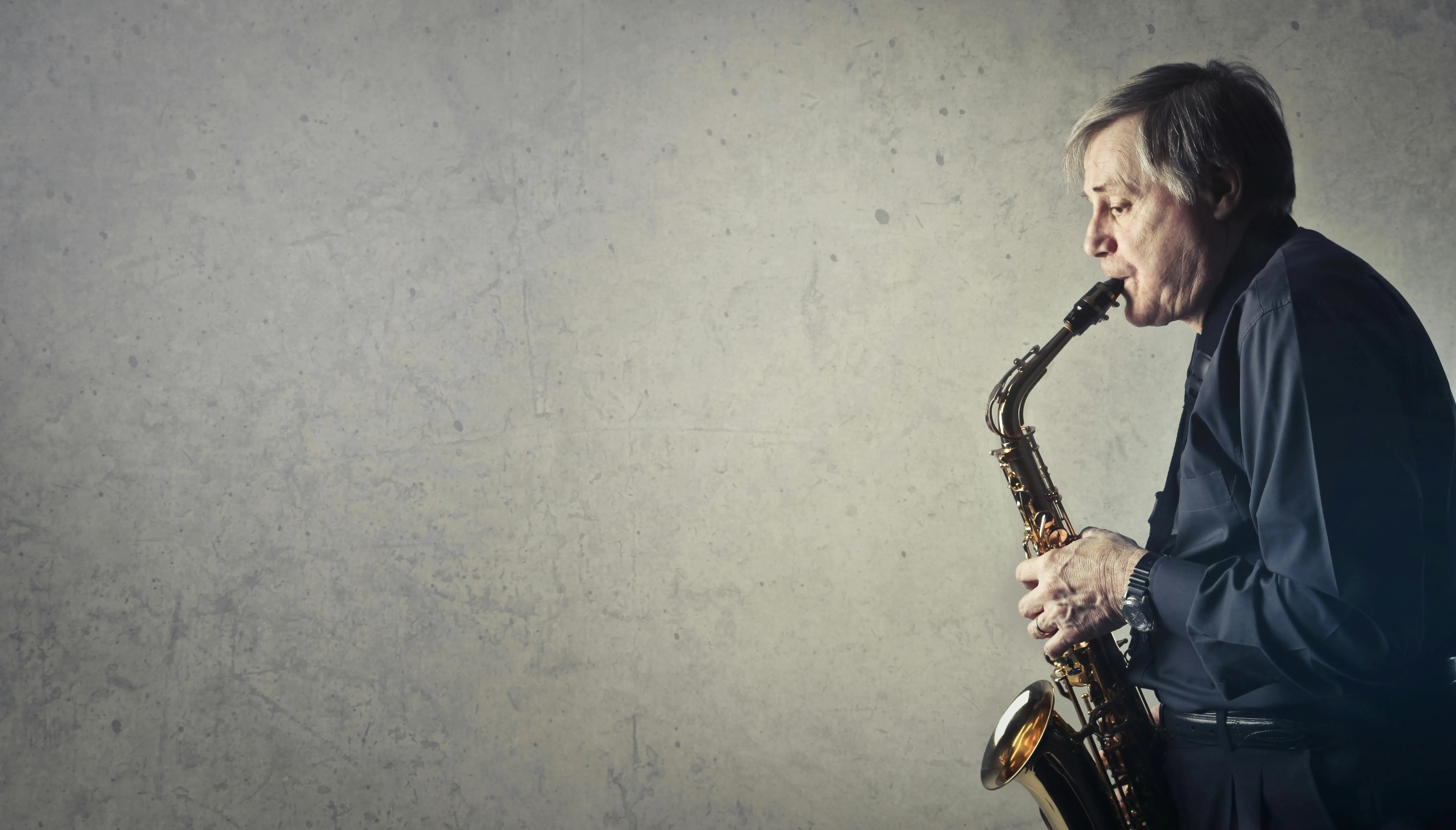 Man playing saxophone against a gray textured wall Wallpaper