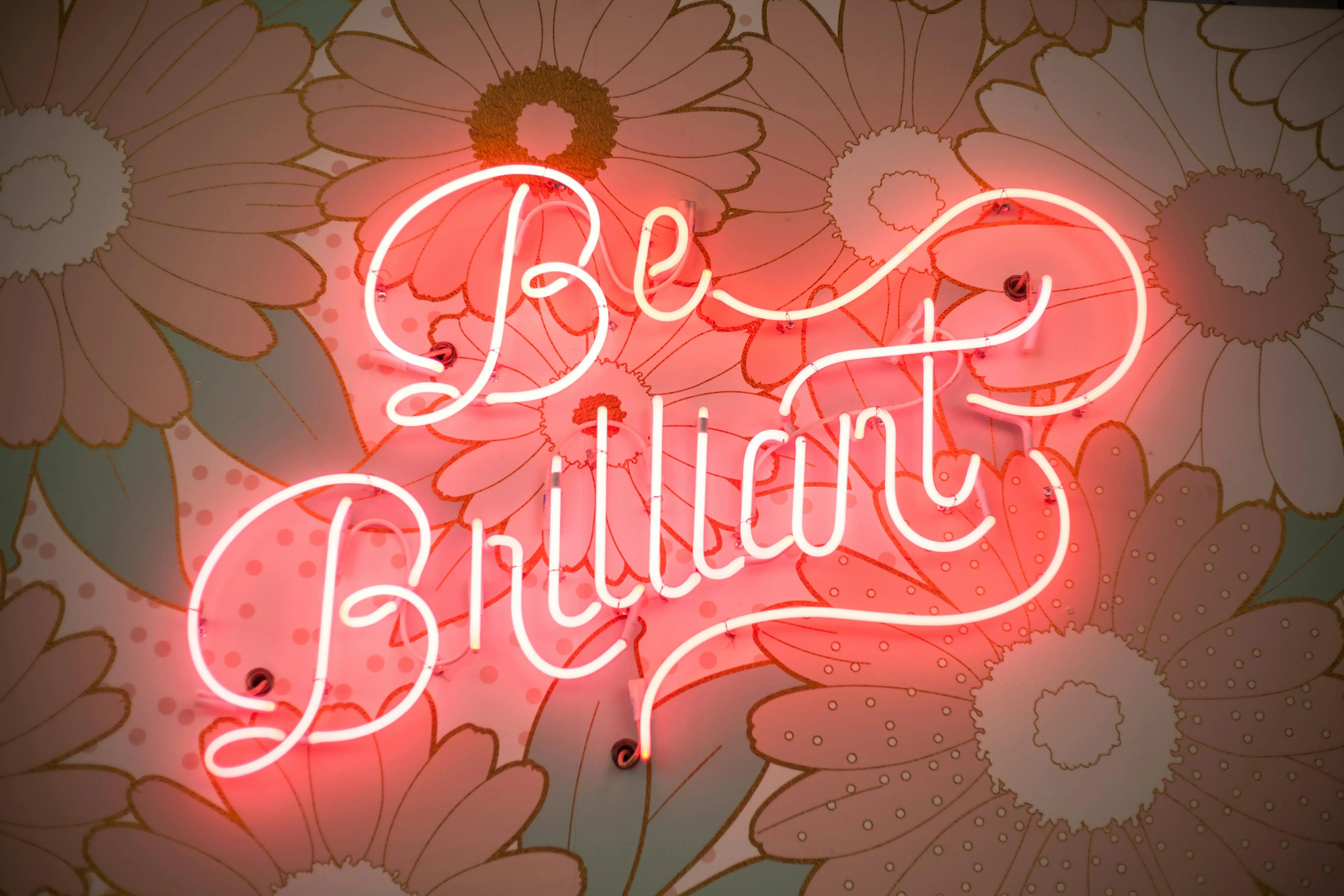 Neon sign saying be brilliant with a floral background 4K