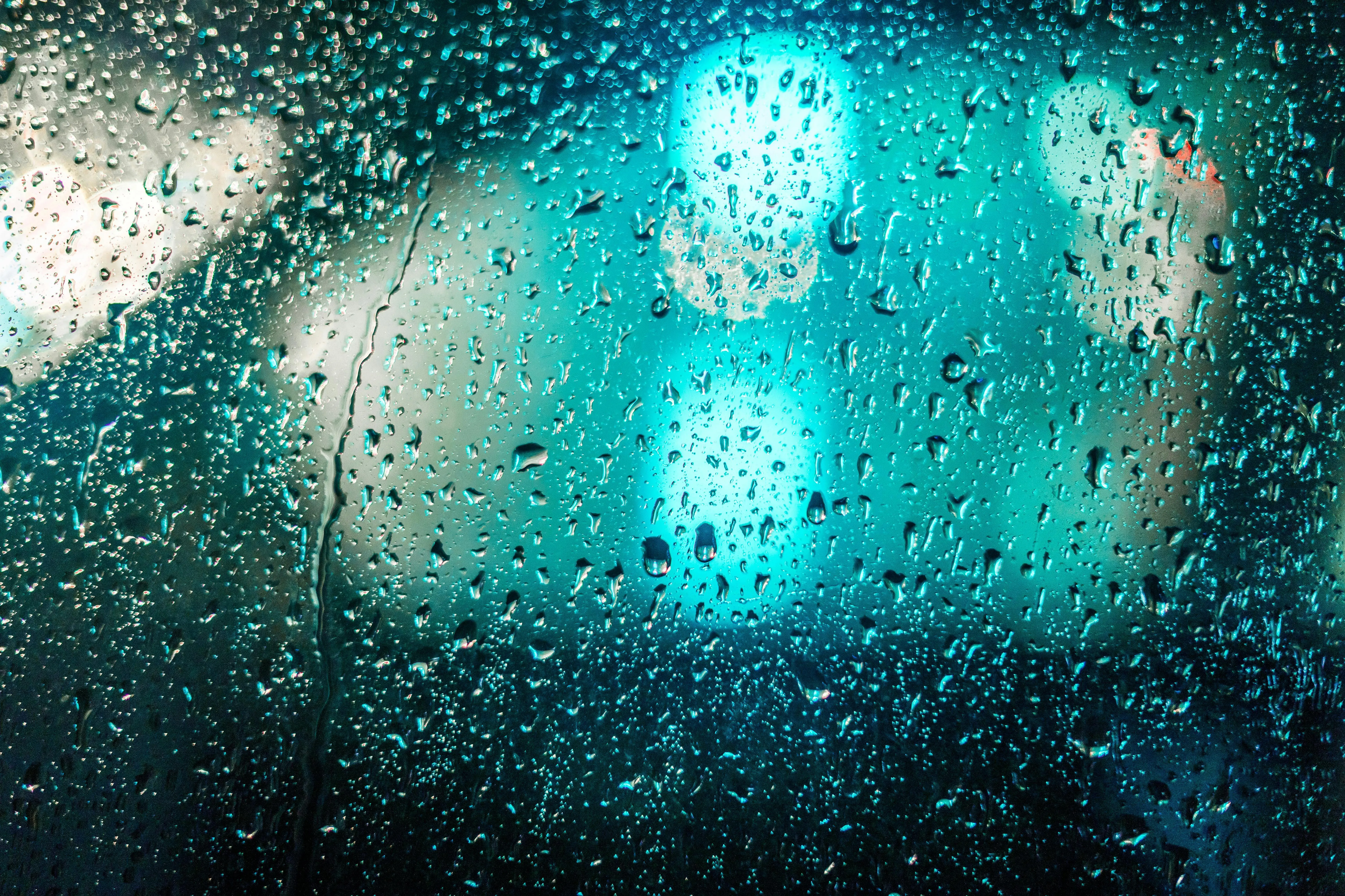 Raindrops on window glass with blurred blue and green lights