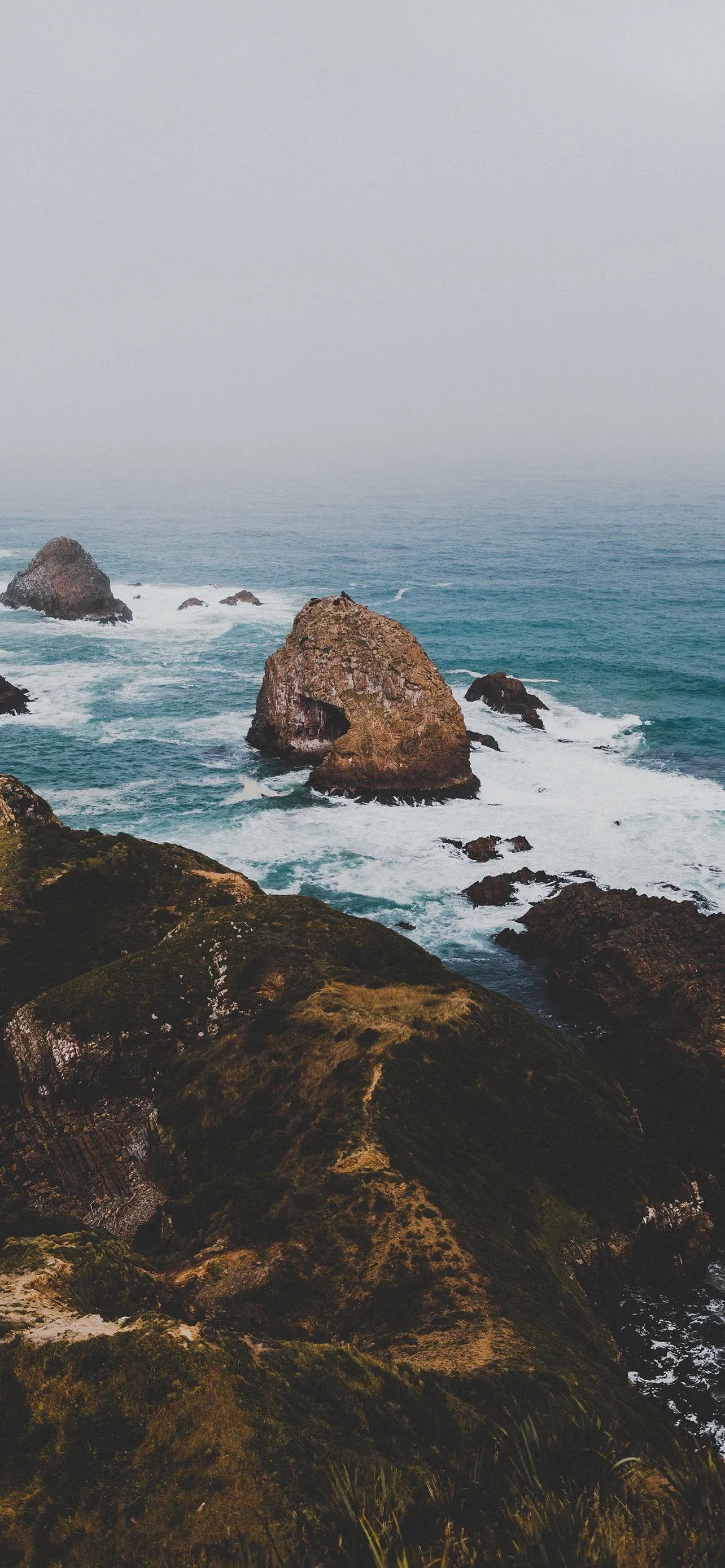 Rocky Shoreline with Ocean View and Cloudy Skies Wallpaper
