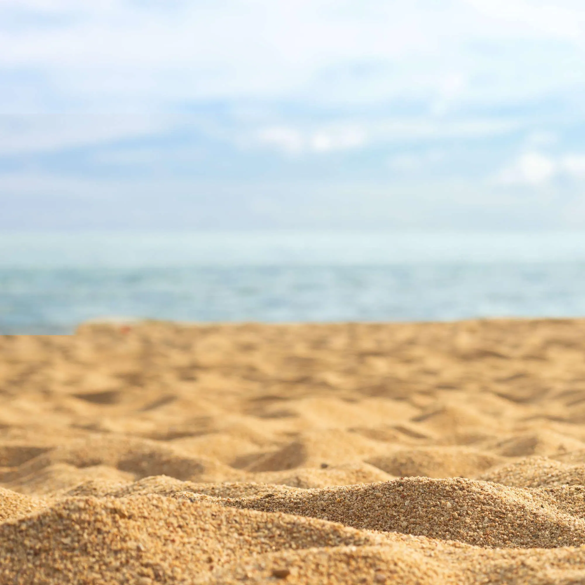 Sandy beach close up with soft ocean waves in the distance