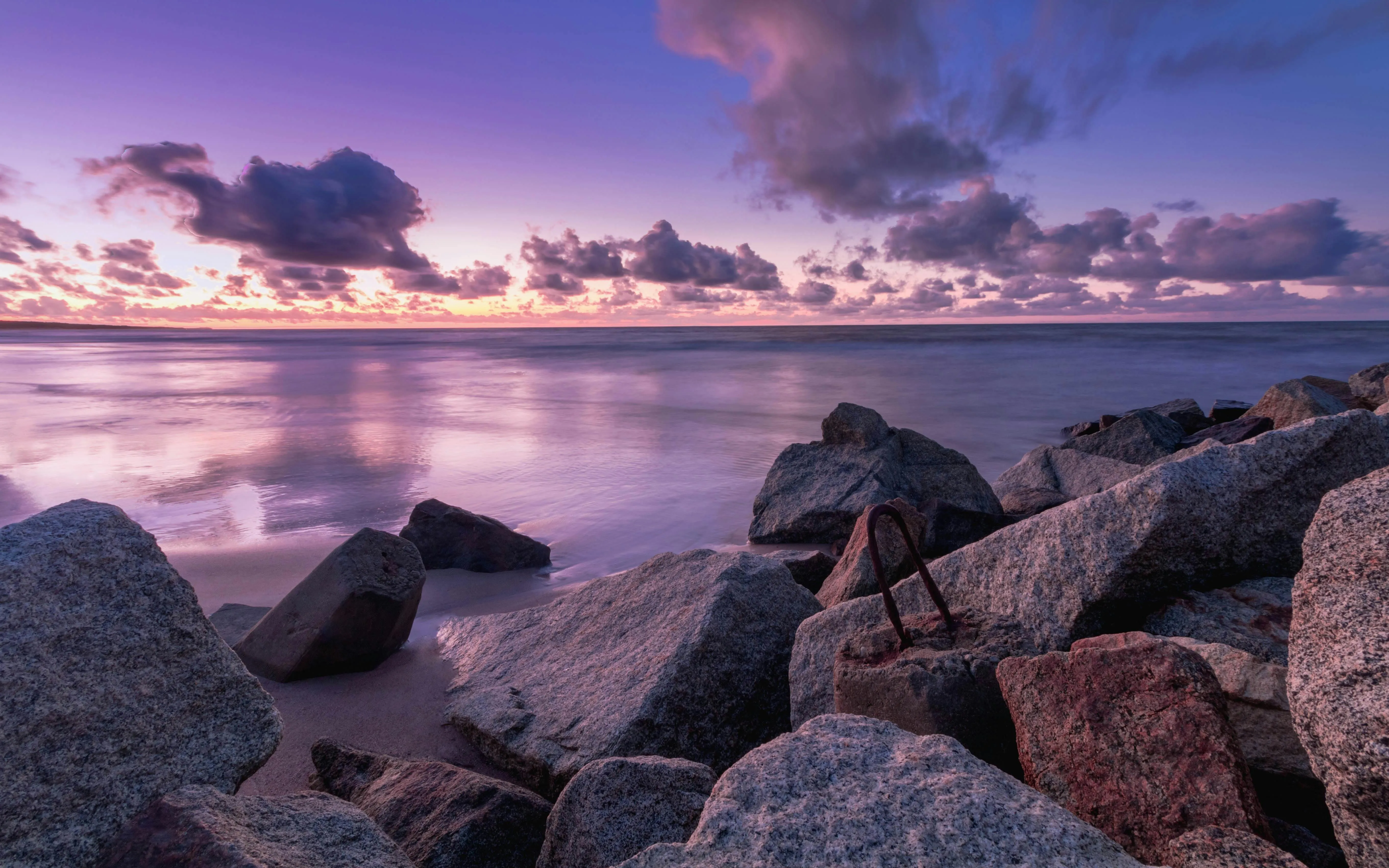 Seashore with rocks under a purple and pink sunset sky HD