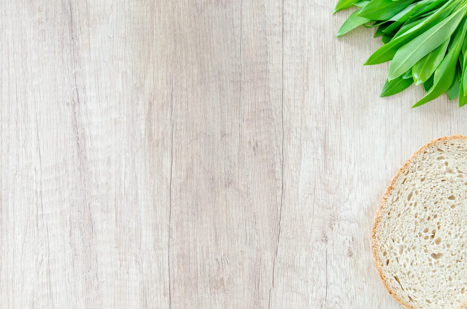 Slice of bread and fresh greens on a white wooden table