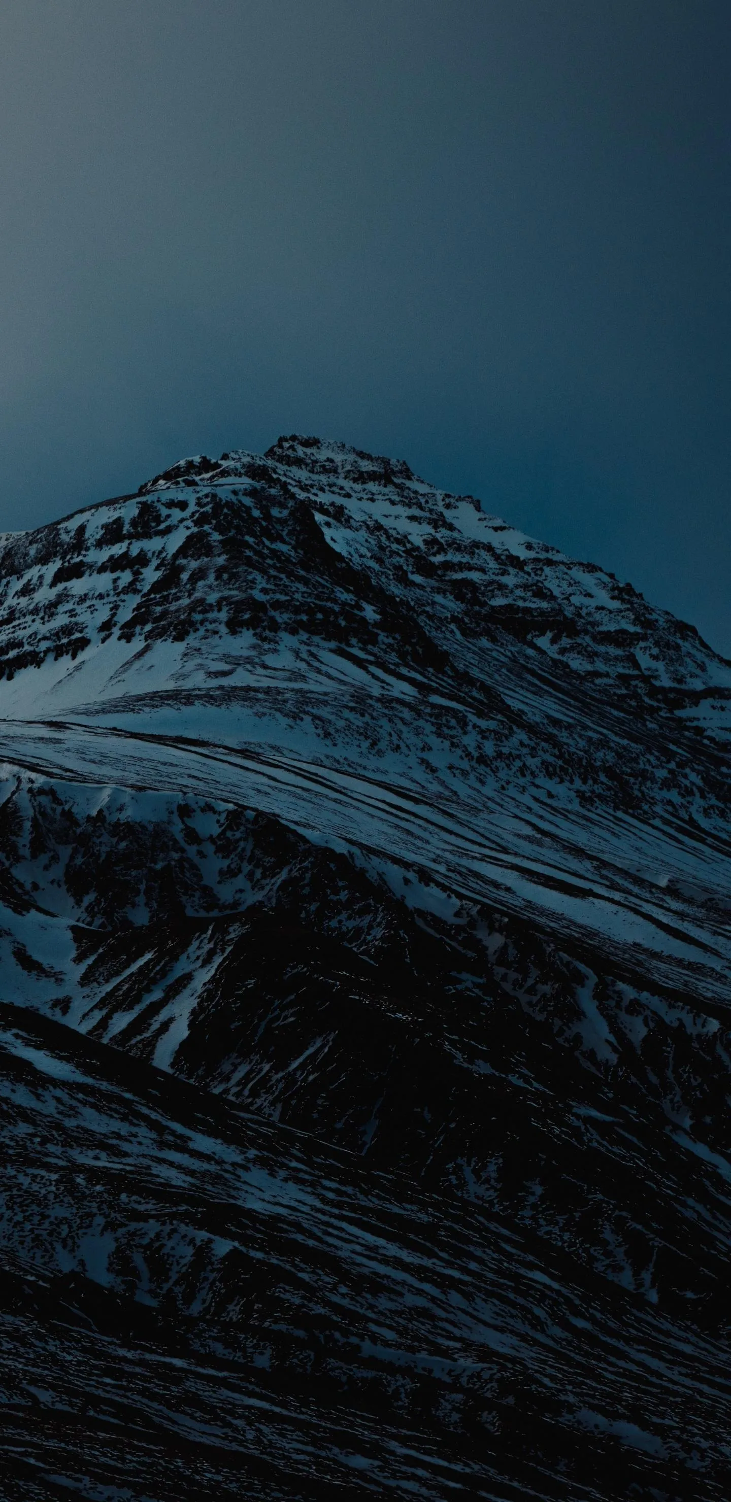 Snow covered mountain peak against moody sky Wallpaper