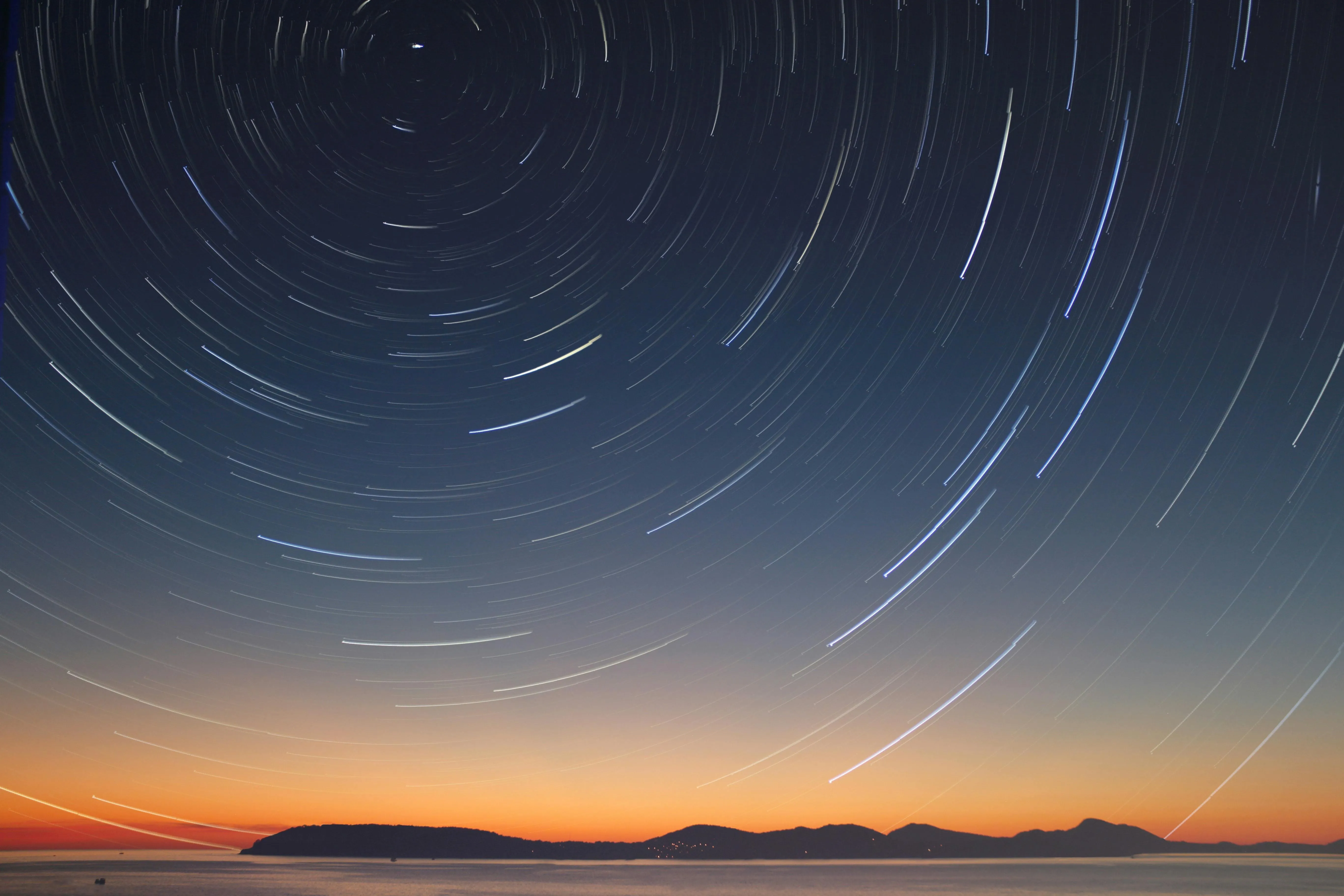 Star trails over dark horizon with orange sunset glow image