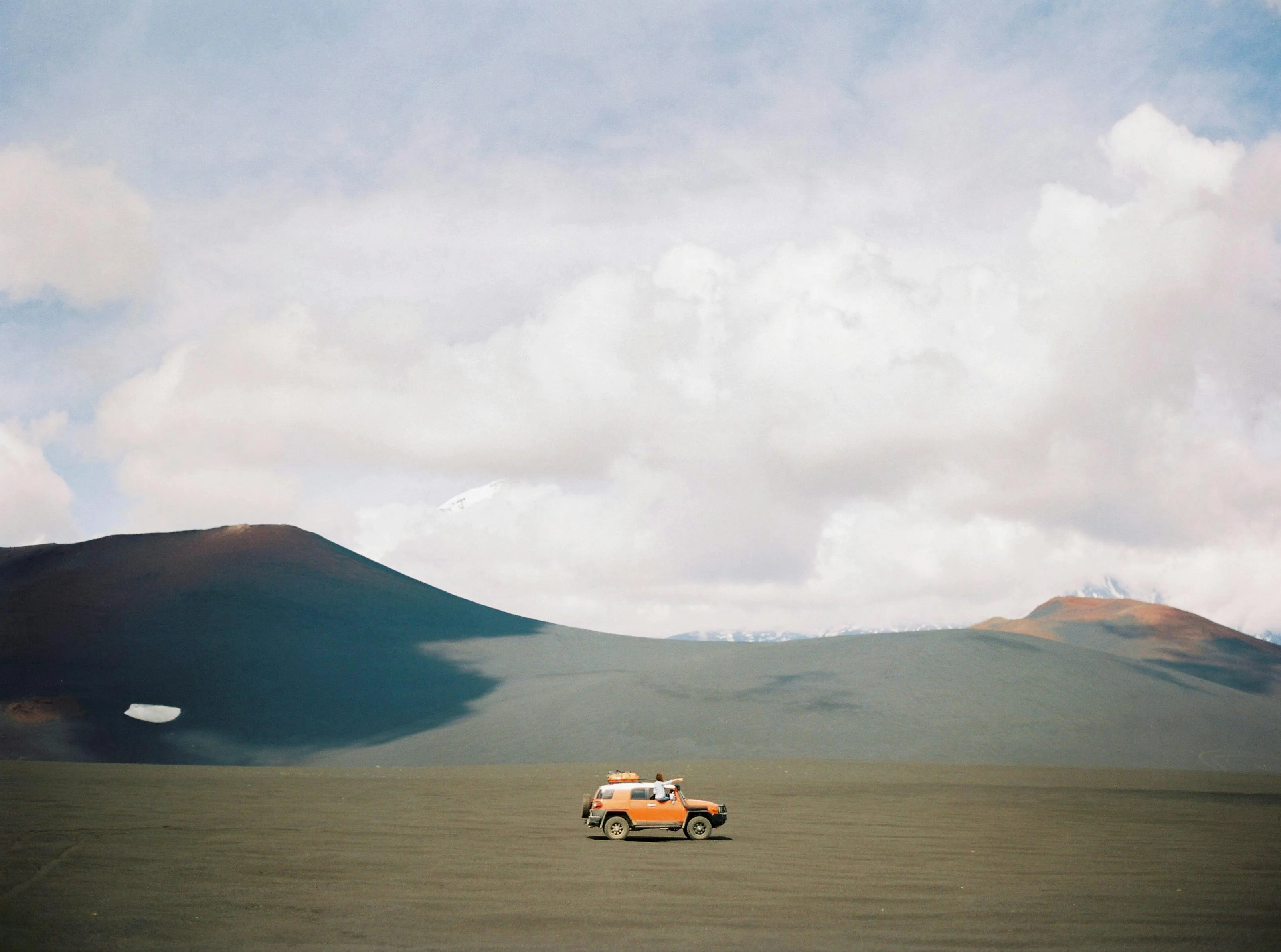 SUV driving across black volcanic sand under cloudy sky