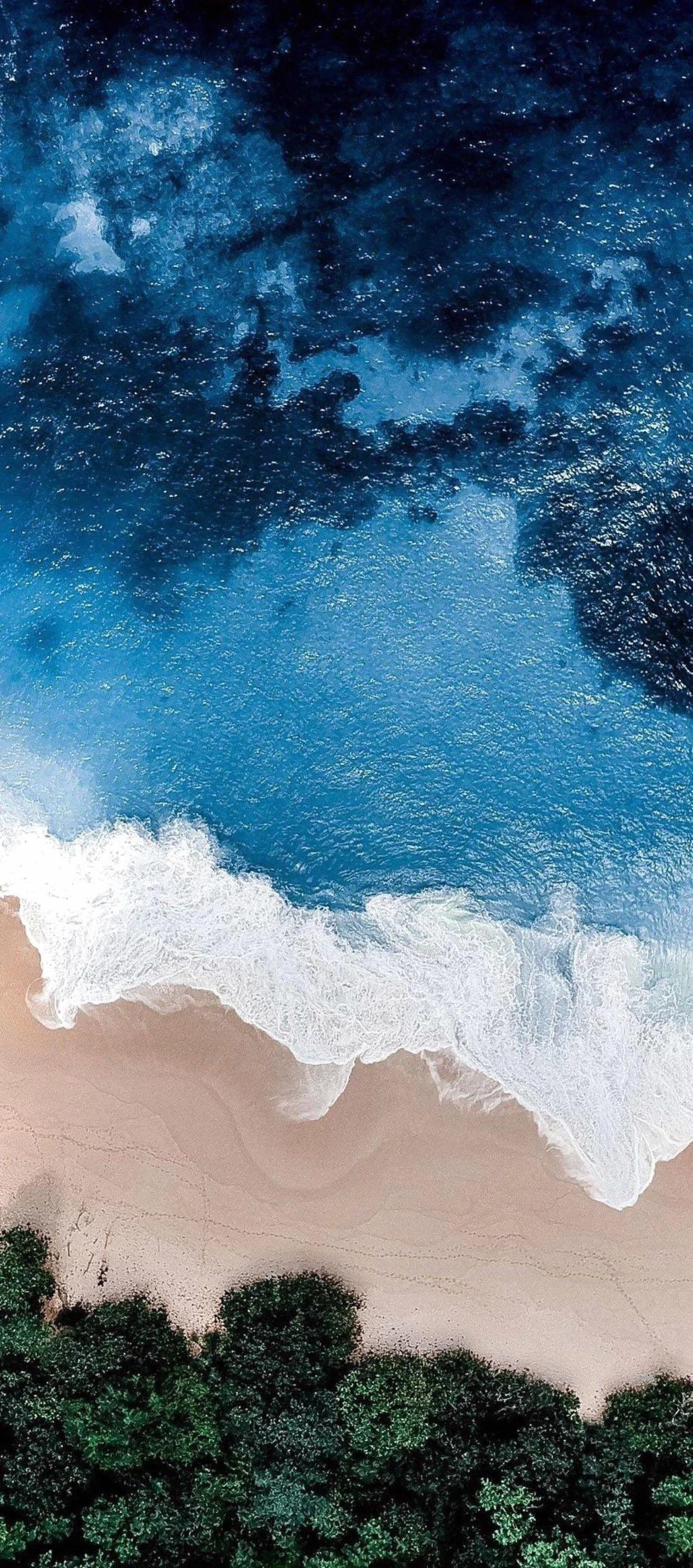 Top view of ocean waves hitting a sandy shoreline Wallpaper