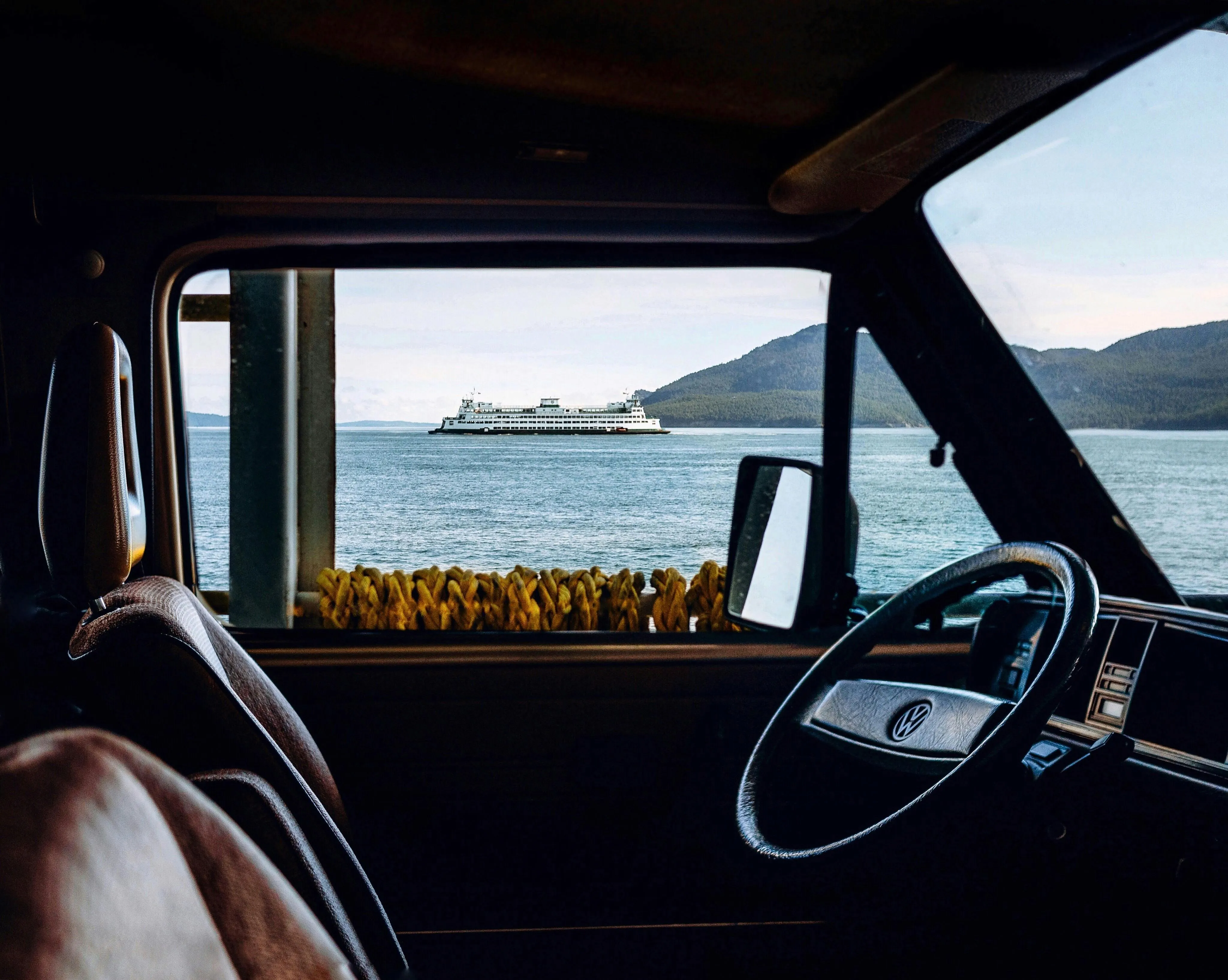 View from inside a car showing an ocean ship and a mountain