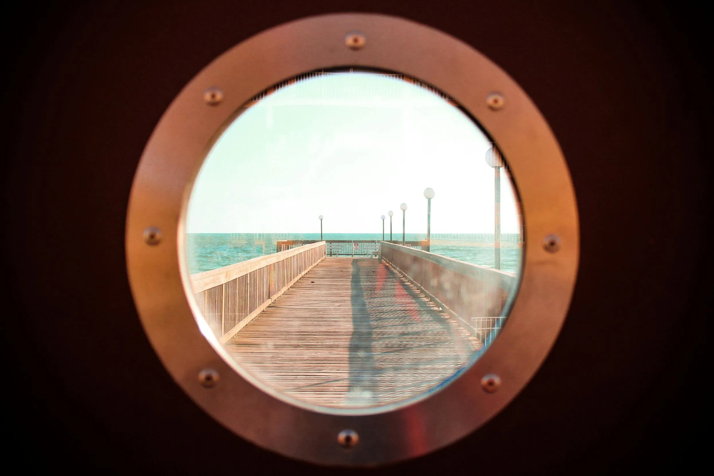 View of a pier through a round ship porthole window HD image