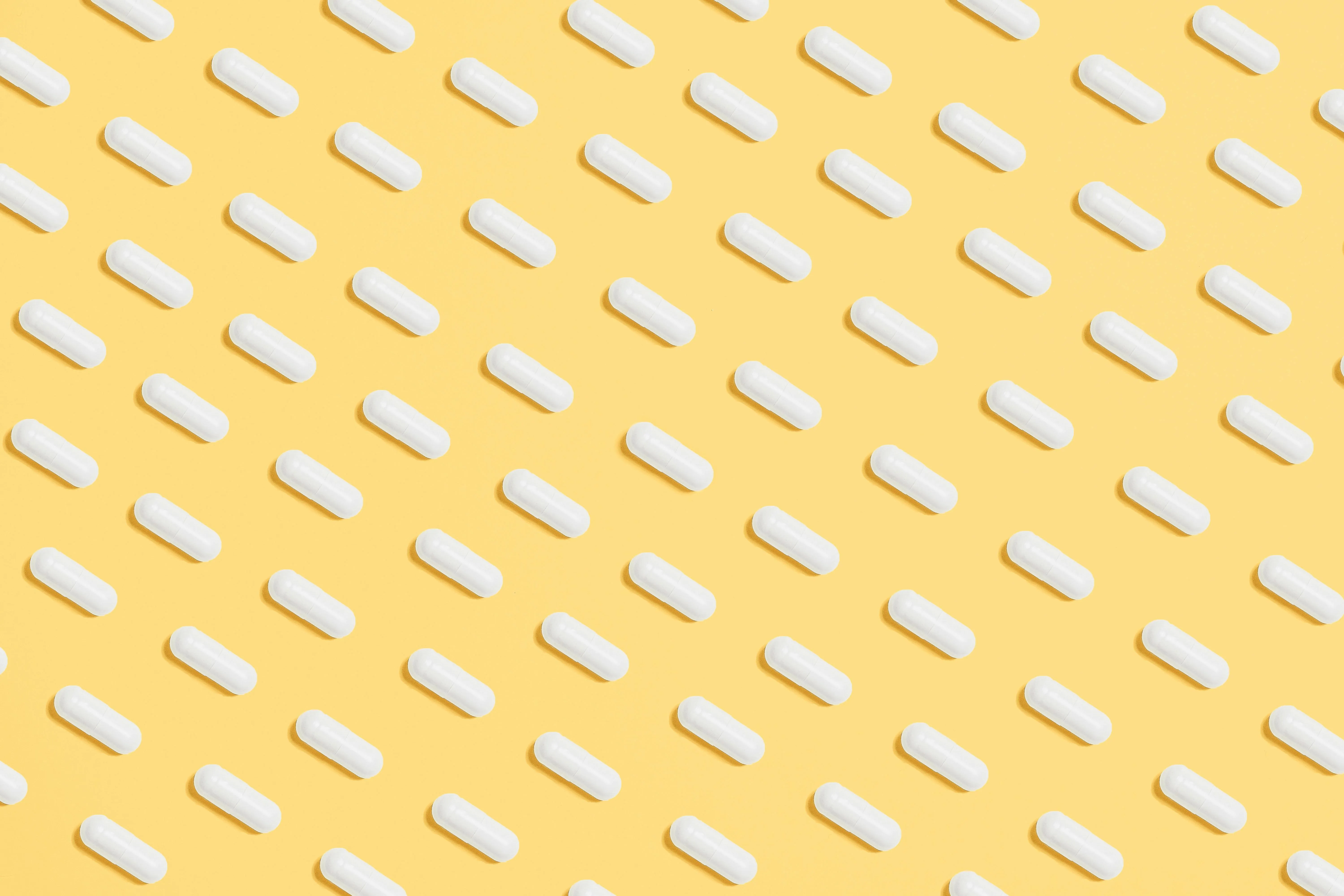 Yellow background with white and pink capsule pills pattern
