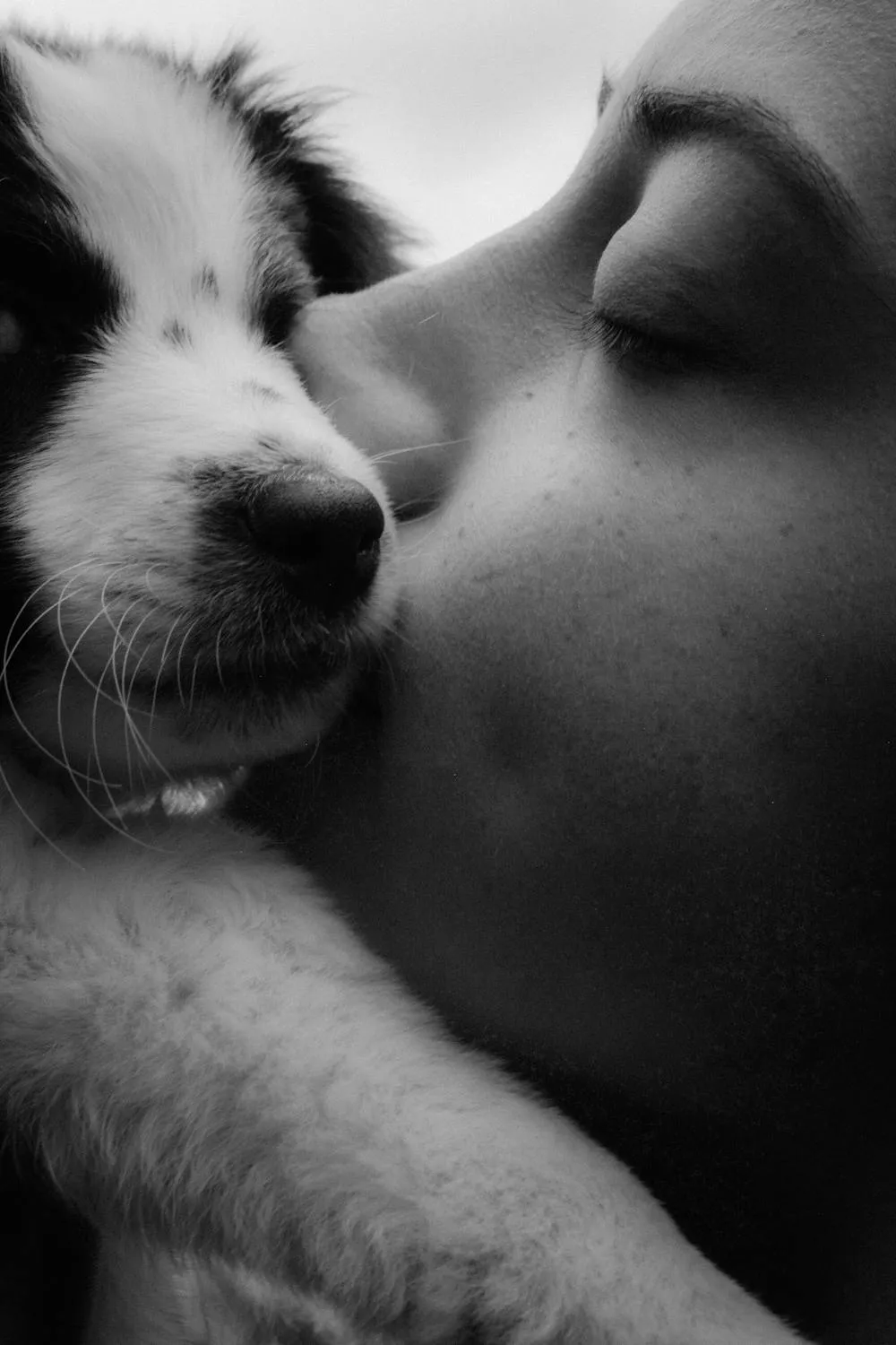 Black and White Photo Of a Woman Kissing a Fluffy Puppy