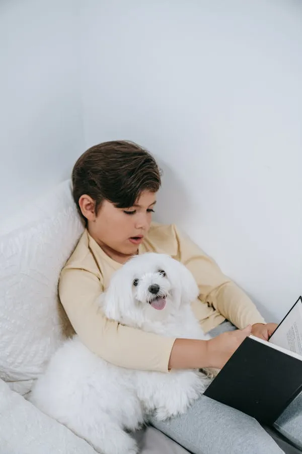 Boy Reading a Book By Hugging a Fluffy White Puppy Closely