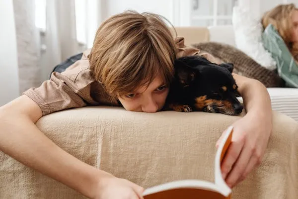 Child Reading Book with Small Dog Resting on Bed Wallpaper