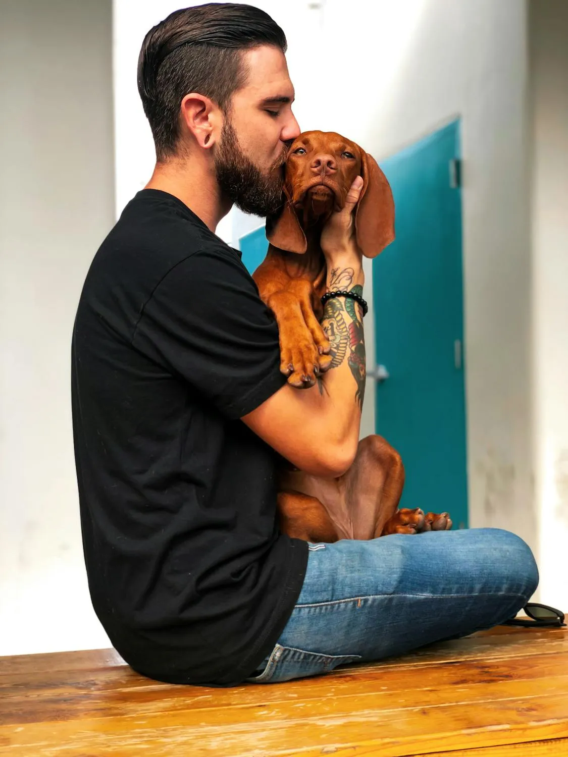Man Kissing Brown Puppy While Sitting on Wood Floor Image