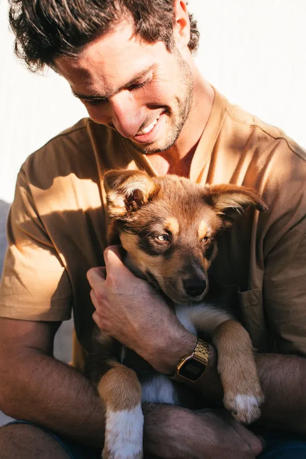 Man Smiling Warmly By Holding An Adorable Brown Puppy
