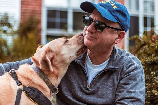Man Wearing Sunglasses Getting a Kiss From His Dog Image