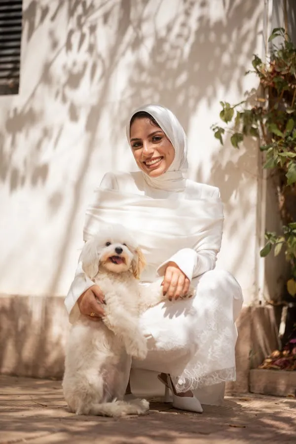 Woman in White Smiling While Holding a Cute White Dog
