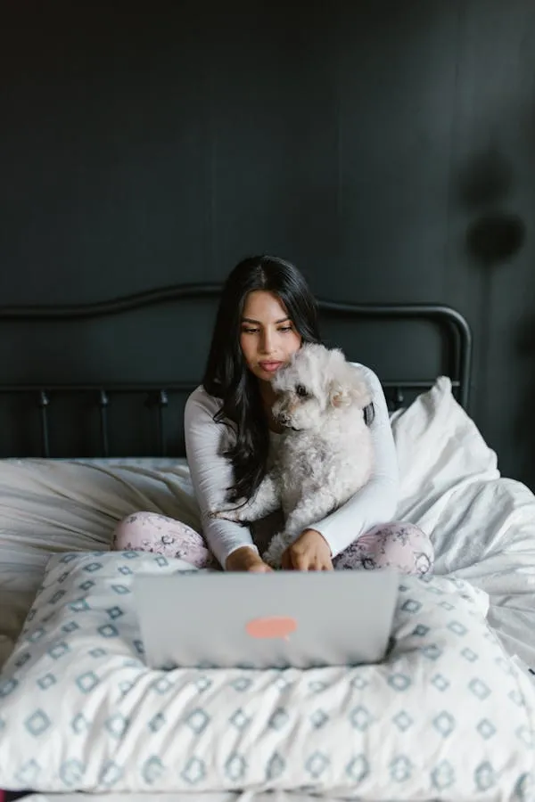 Woman Working on Laptop While Sitting on Bed with Puppy