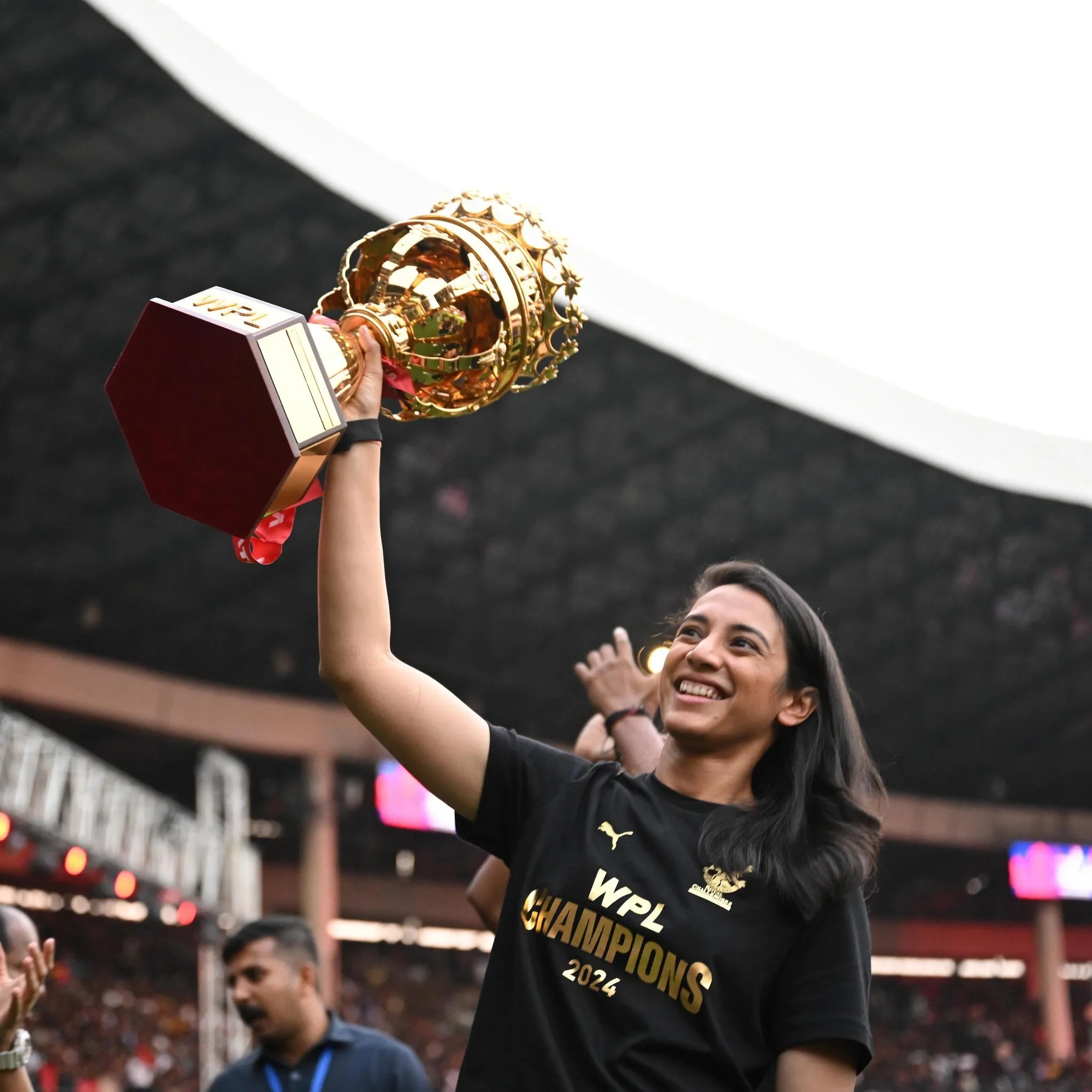 Smriti Mandhana lifting a trophy in celebration on stage