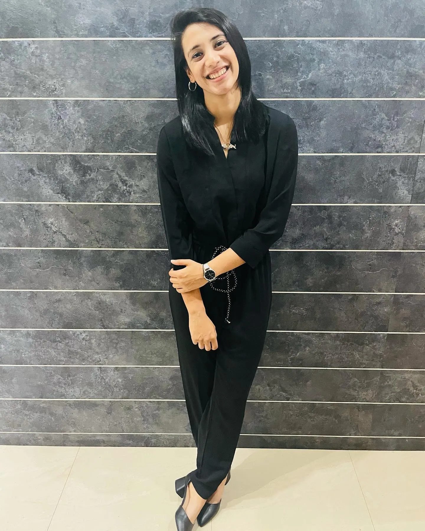 Smriti Mandhana posing in black outfit near stone wall