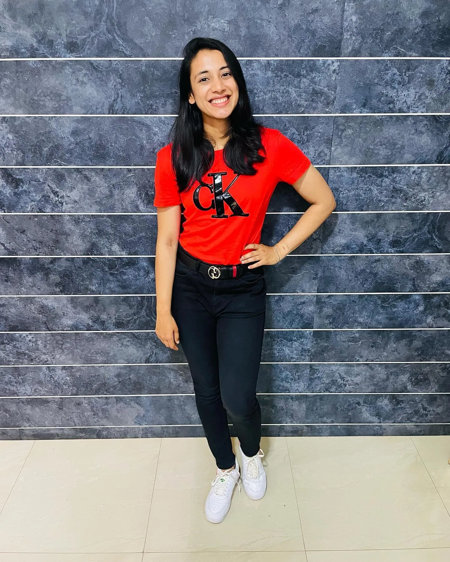Smriti Mandhana posing in red top and black jeans indoors