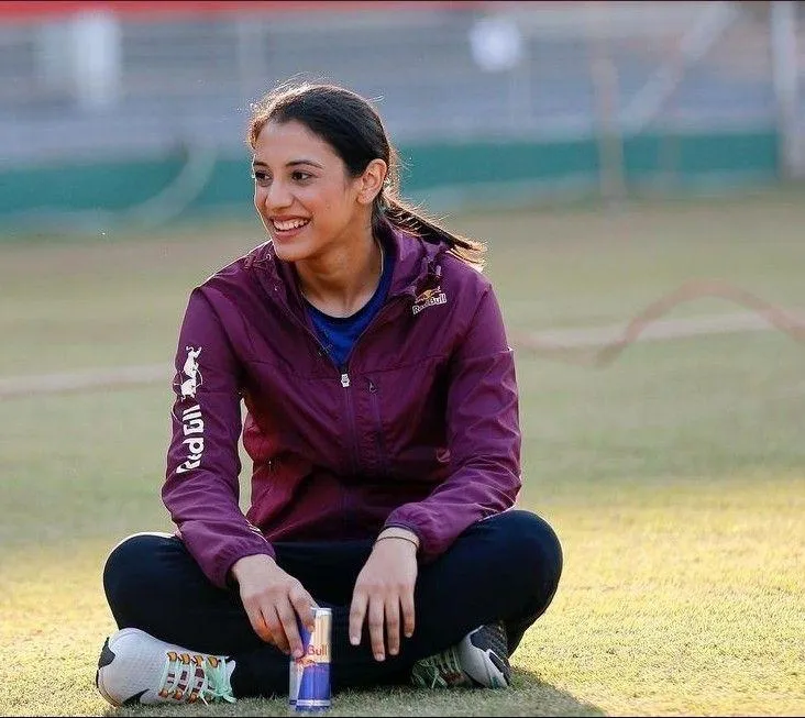Smriti Mandhana seated on field in maroon hoodie wallpaper