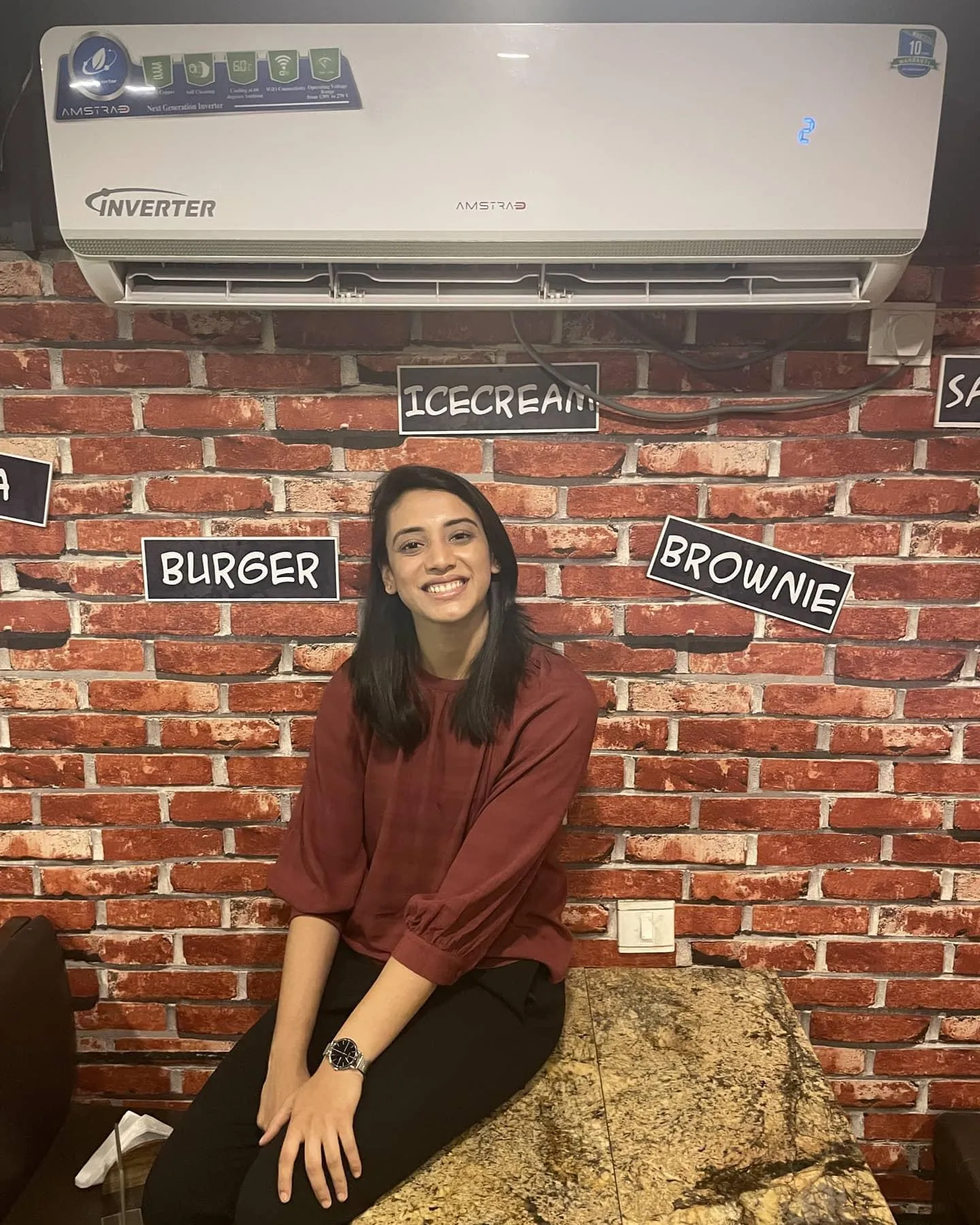 Smriti Mandhana sitting by red brick wall in casual clothes