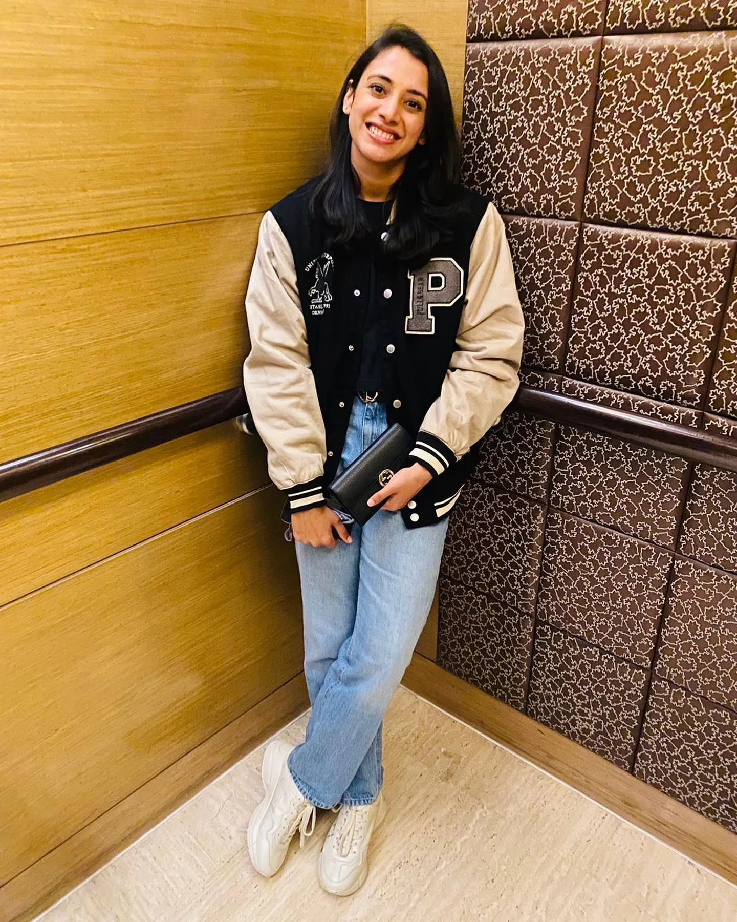 Smriti Mandhana sitting by wall in jeans and brown sweater