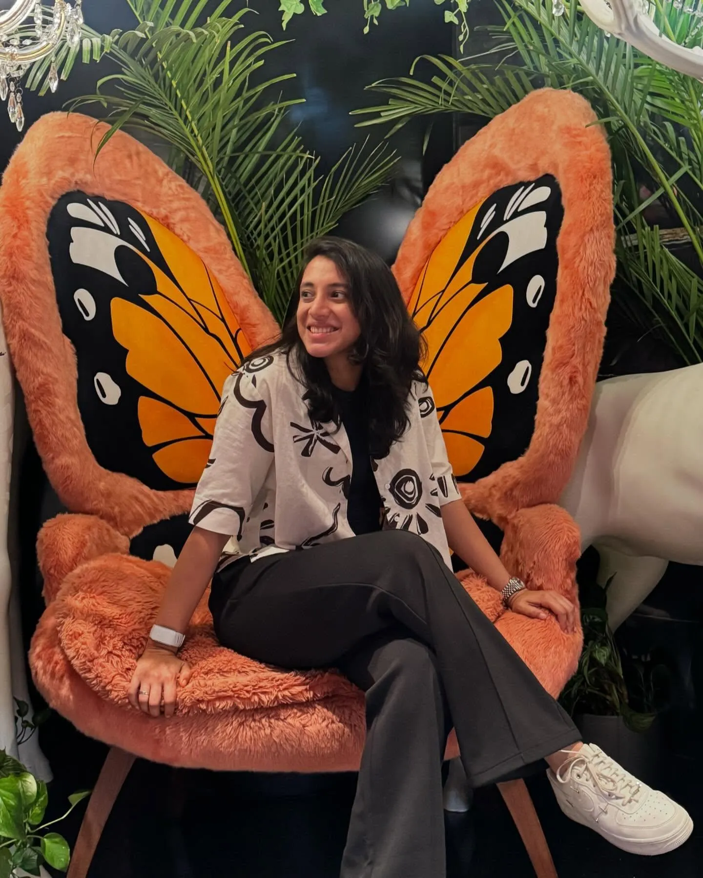 Smriti Mandhana sitting on a bench butterfly wings behind her