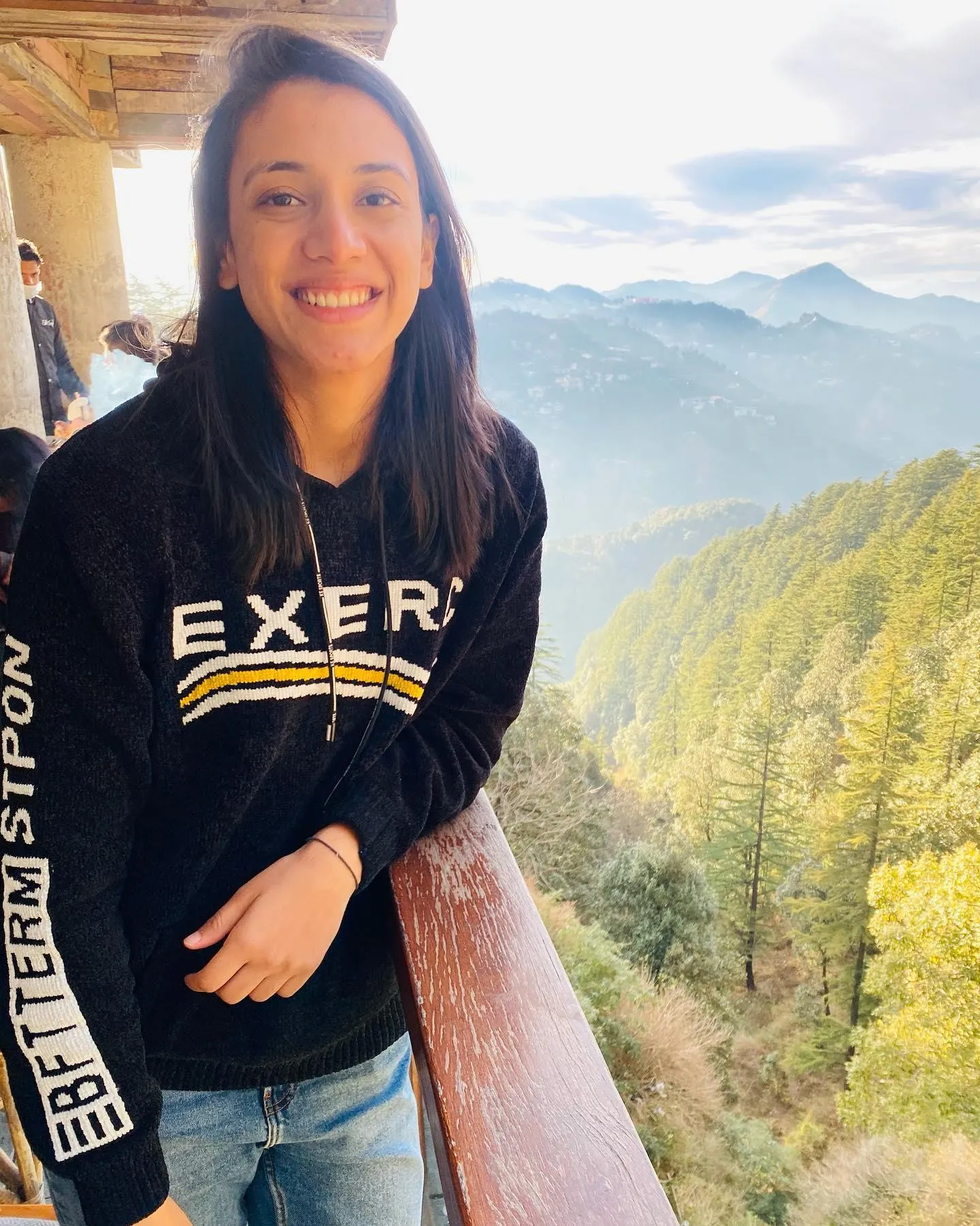Smriti Mandhana smiling in black SKFM shirt on a trail