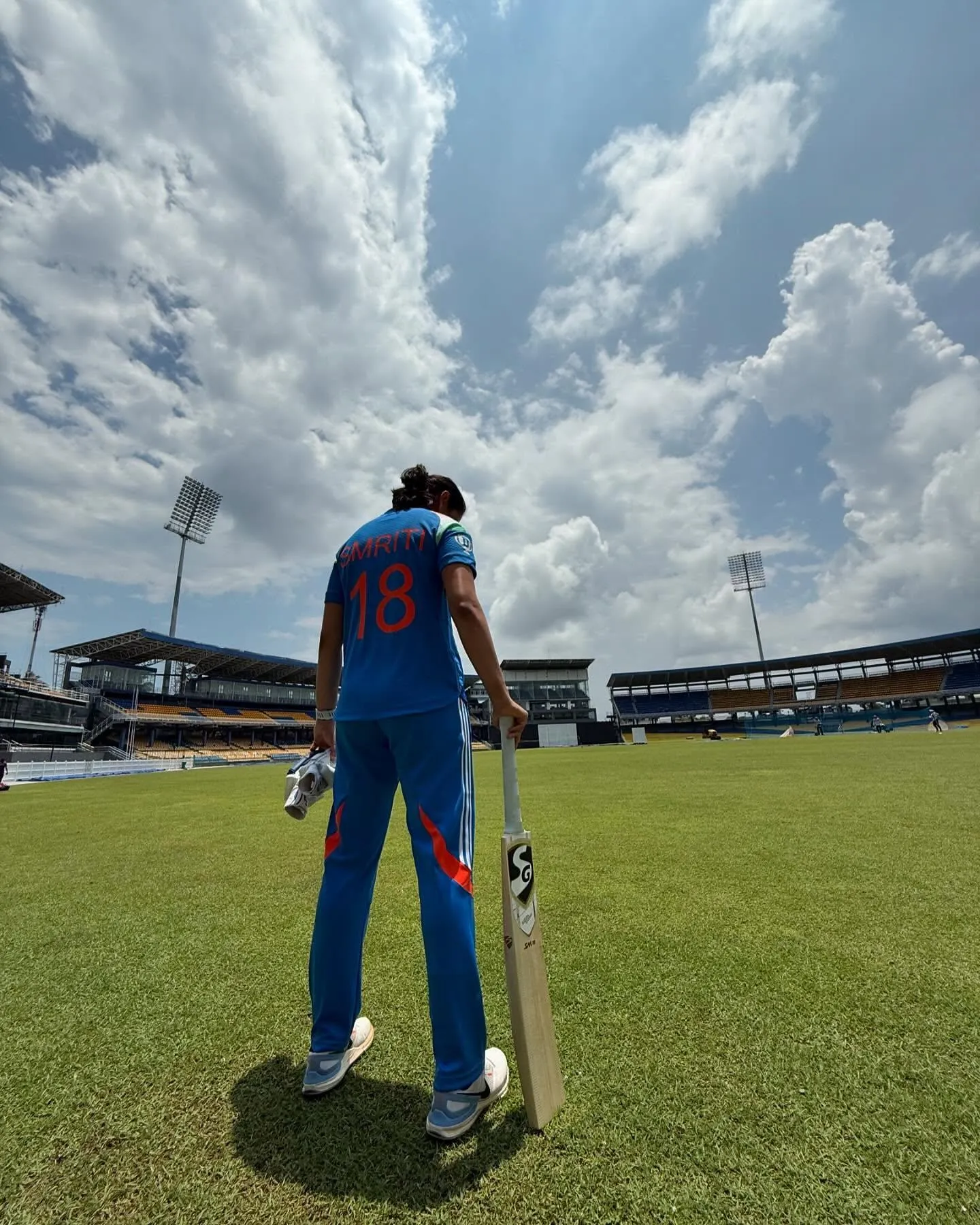 Smriti Mandhana standing tall on a bright green cricket field