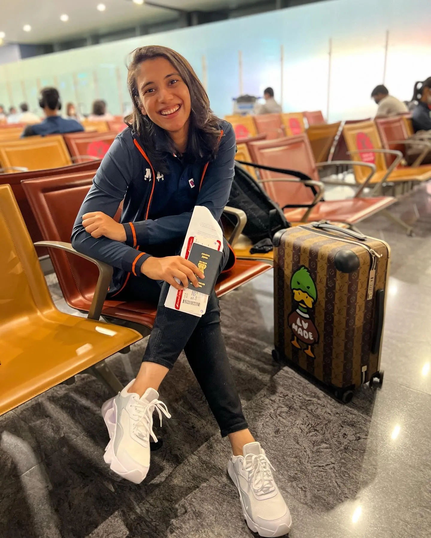 Smriti sitting casually with luggage in a waiting area