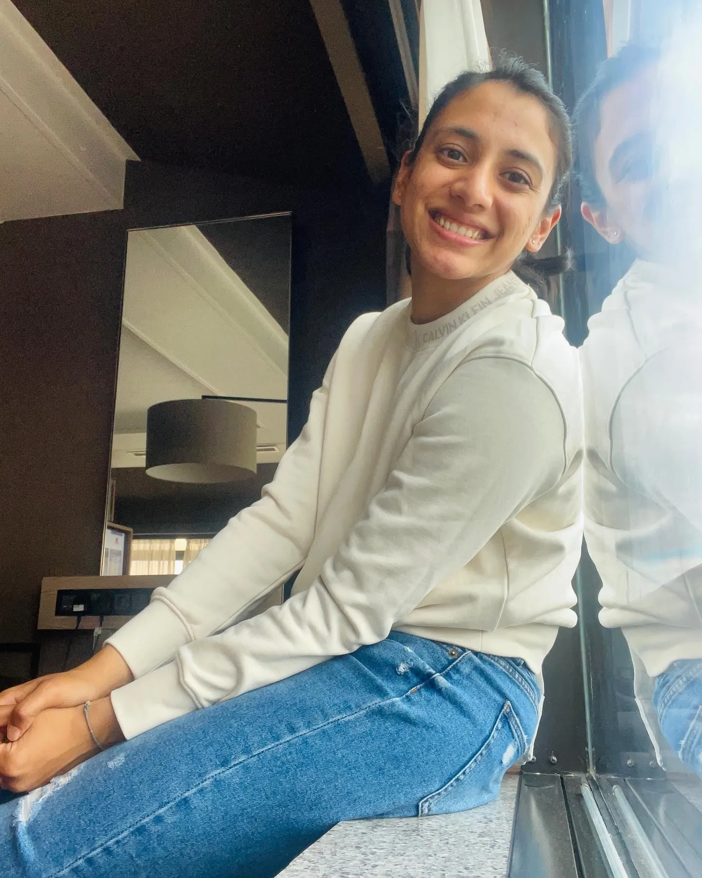 Smriti sitting indoors in white shirt and jeans smiling