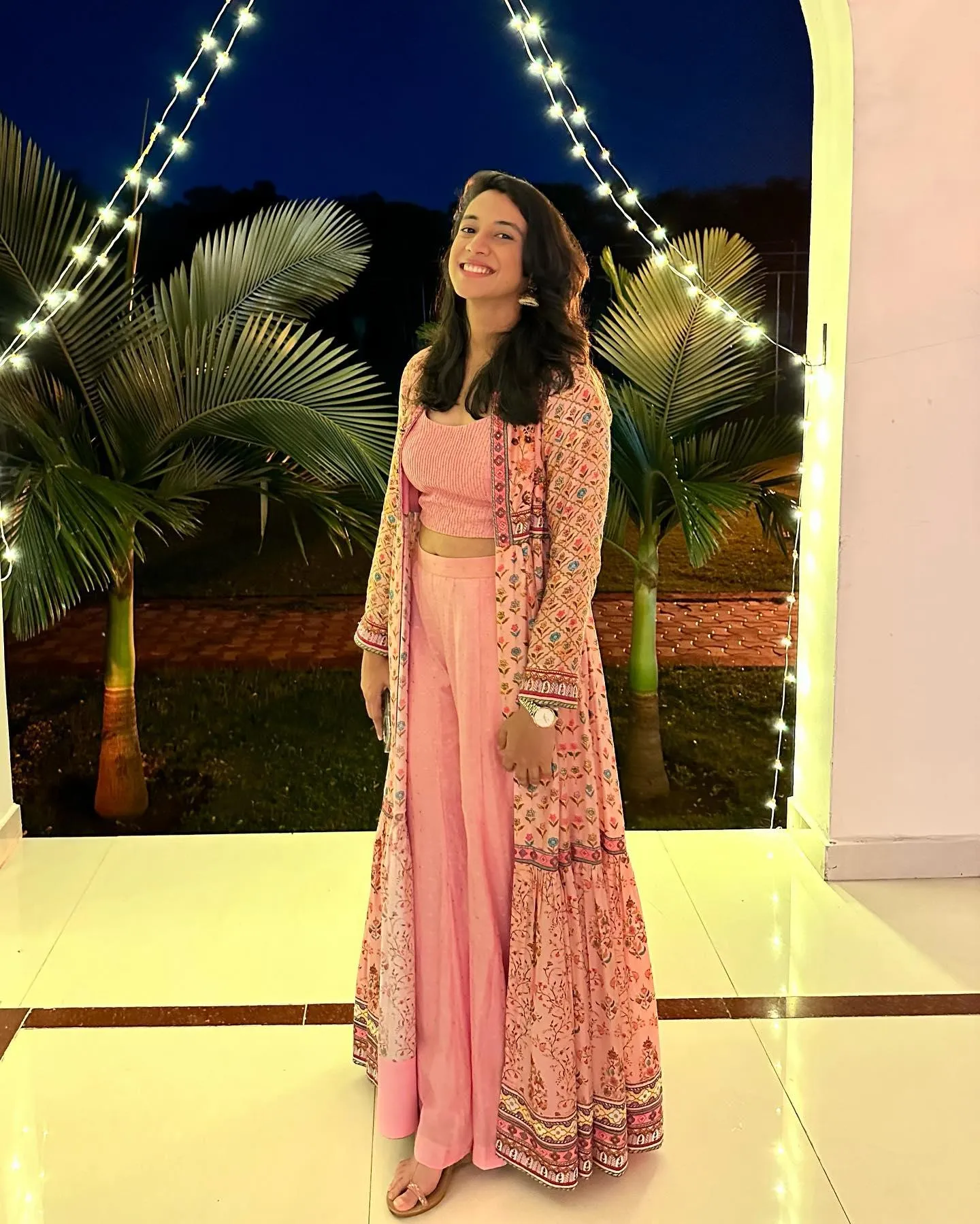 Smriti standing in a pink dress on a lit staircase