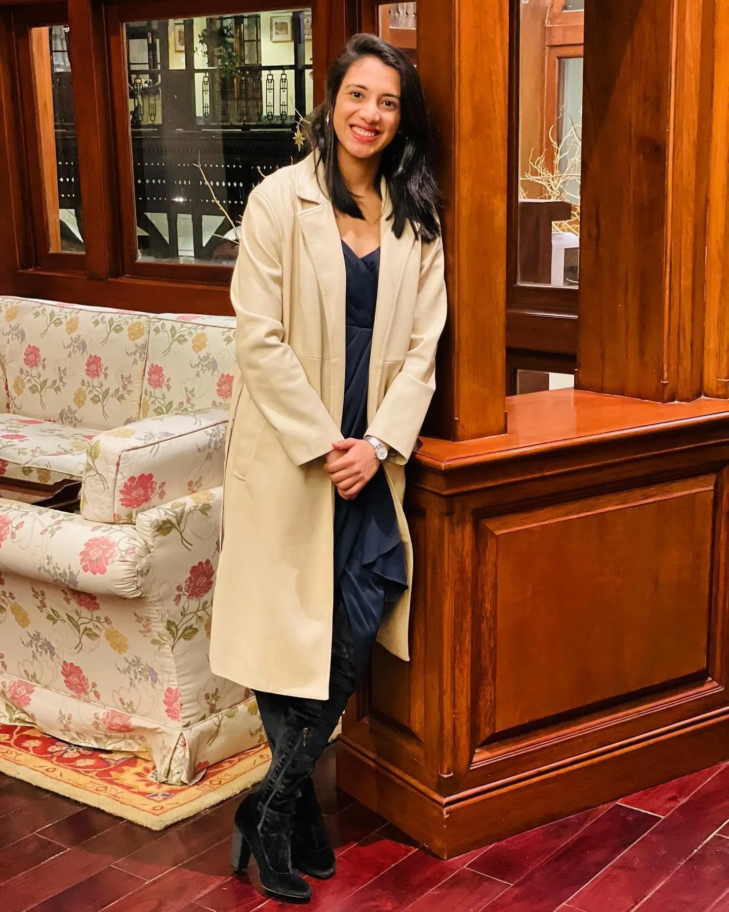 Smriti standing near a mirror in a cream colored coat