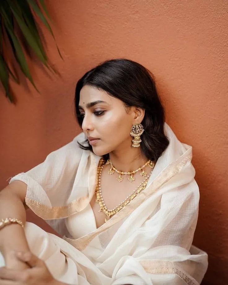 Aishwarya Lekshmi in a white saree lying on the orange wall