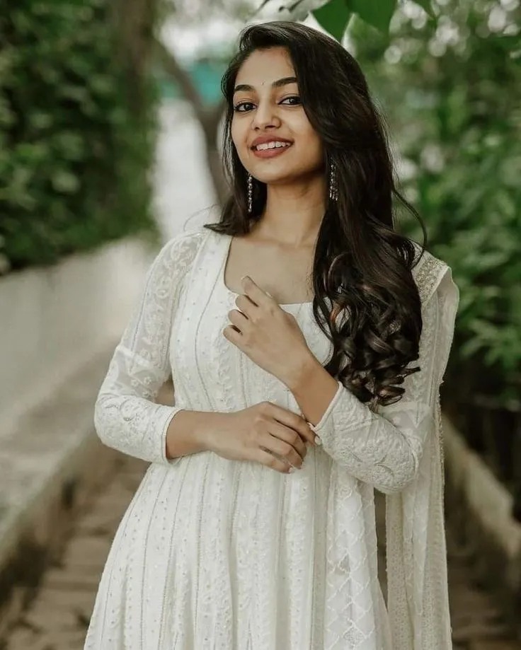 Aleena Shaji in a white dress standing outdoors with a smile